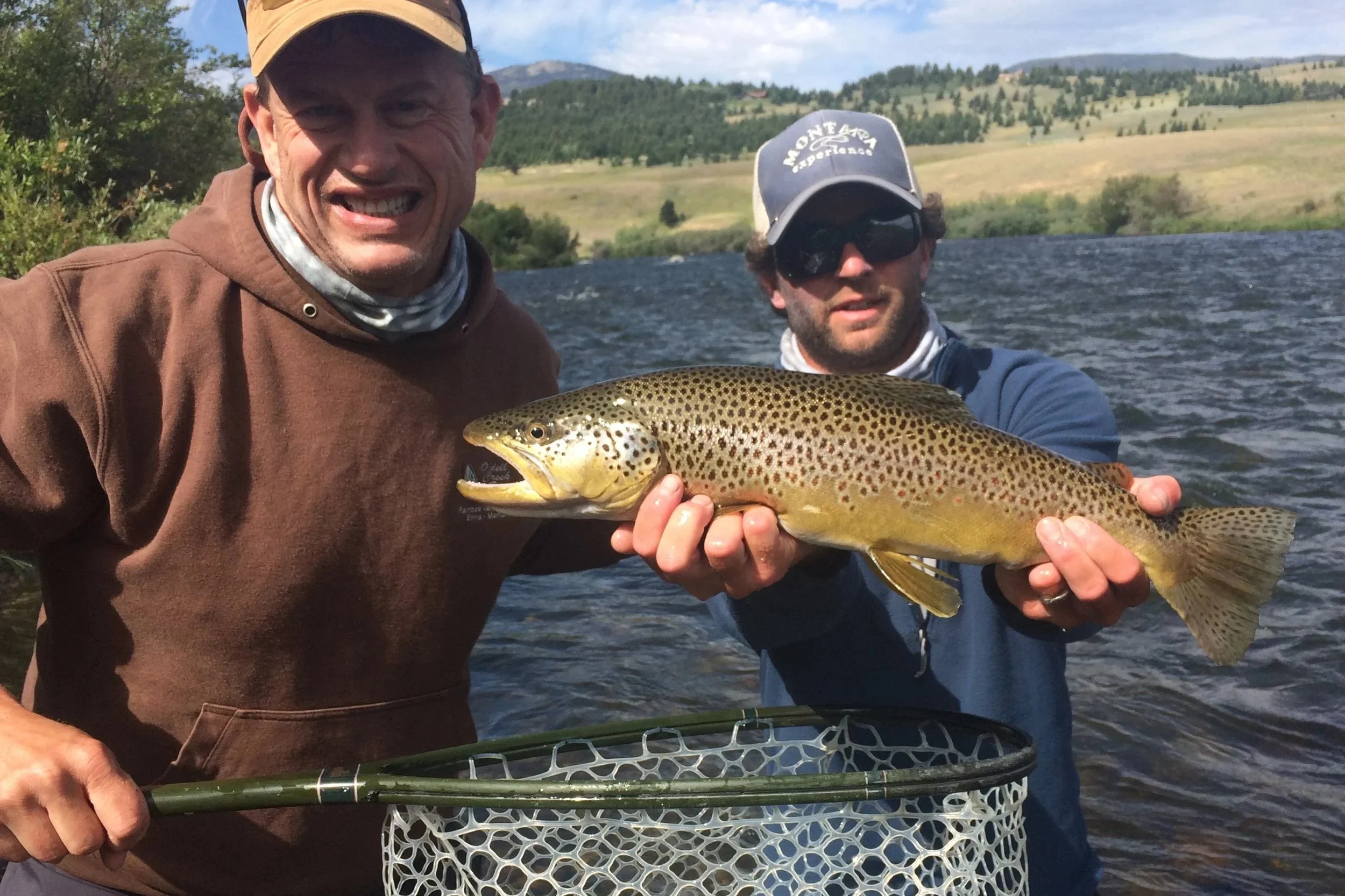 A Flyshot Outfitters guide holding a large wild brown trout for a smiling client just below the Sun West Ranch bridge on the Upper Madison River.