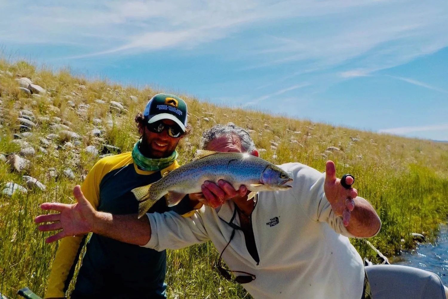 Flyshot Outfitters guide David Kern shares a laugh with a client gesturing the size of a Madison River rainbow trout during a lighthearted day on the water.