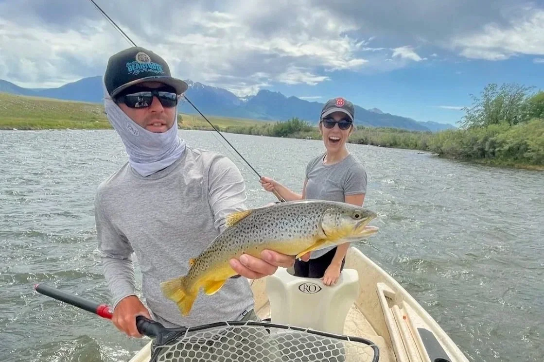 A Five-star review photo from a client on the Madison River, featuring guide David Kern and a smiling guest with a wild brown trout on a Flyshot Outfitters drift boat trip.