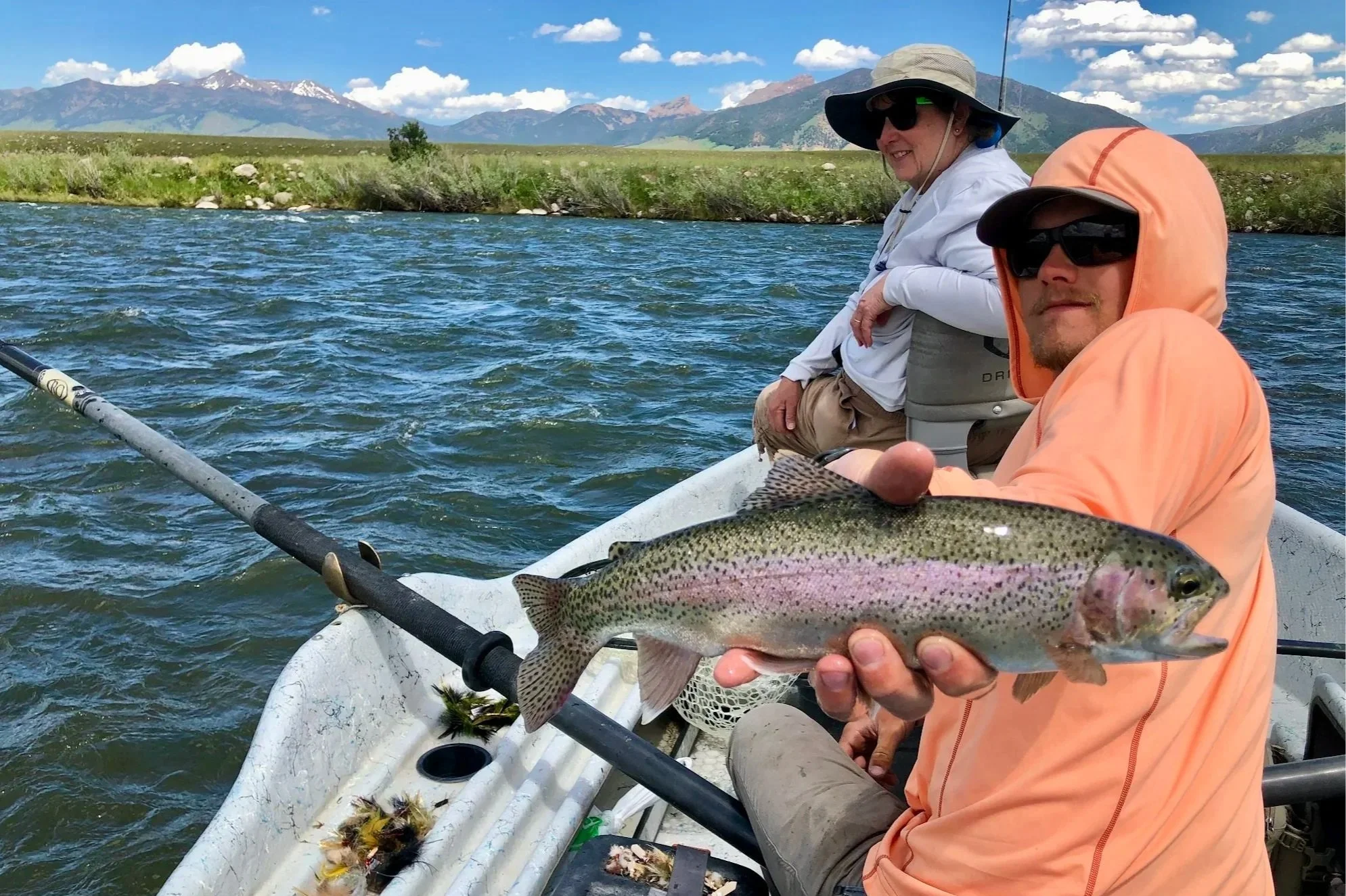 A 5-star review photo featuring Flyshot Outfitters guide River Sterzick holding a Madison River rainbow trout for a smiling client on a professional drift boat trip.