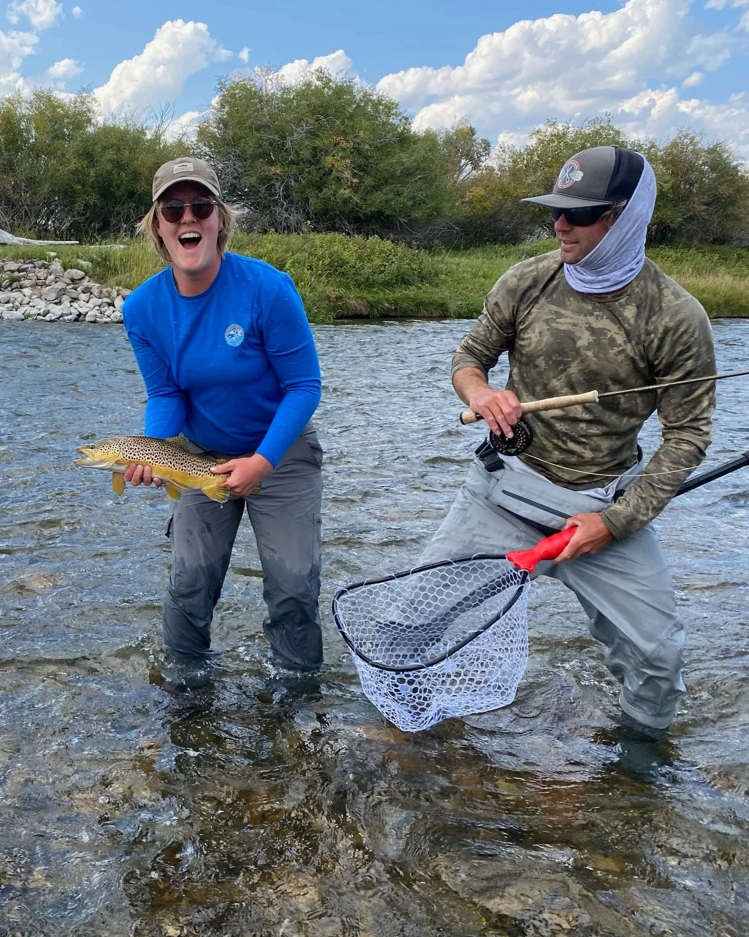 Guided wade fishing in Bozeman: A client smiling with their catch while the Flyshot Outfitters guide assists with a landing net.