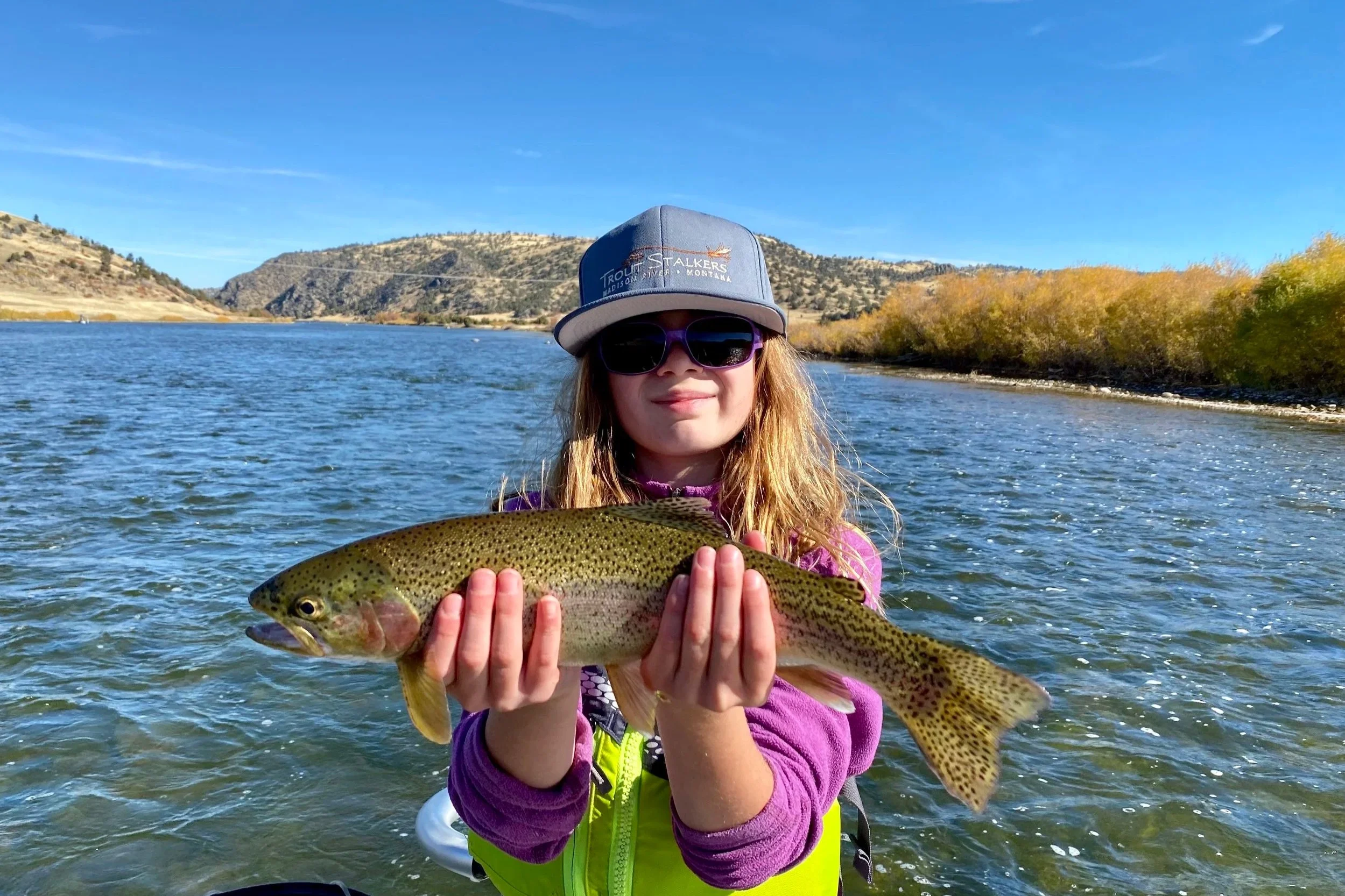 A young girl smiling with a wild Lower Madison River rainbow trout caught during a family-oriented fly fishing trip near Bozeman with Flyshot Outfitters.