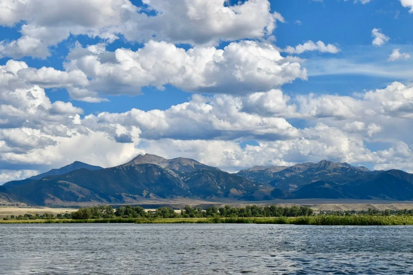 A stunning scenic view looking across Ennis Lake toward the snow-capped Madison Range, highlighting the beautiful landscape of the Madison River valley near Ennis, Montana.