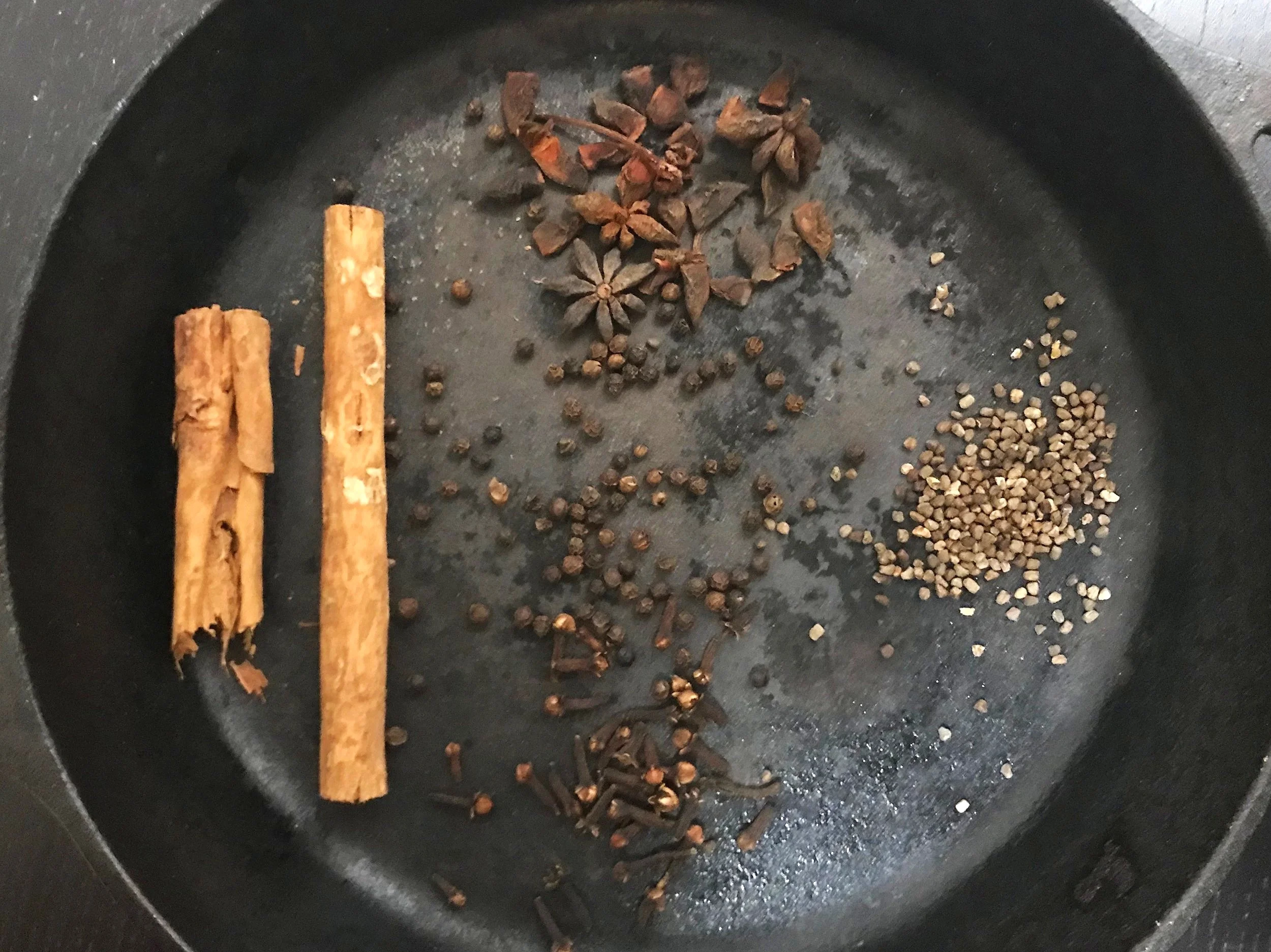From left to right, clockwise: cinnamon sticks, star anise, cardamom, cloves. Center: peppercorn
