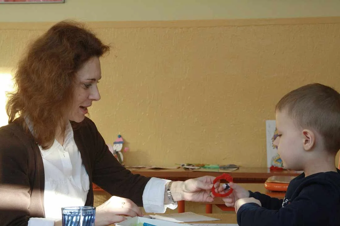 Female teacher making crafts with young boy in a classroom