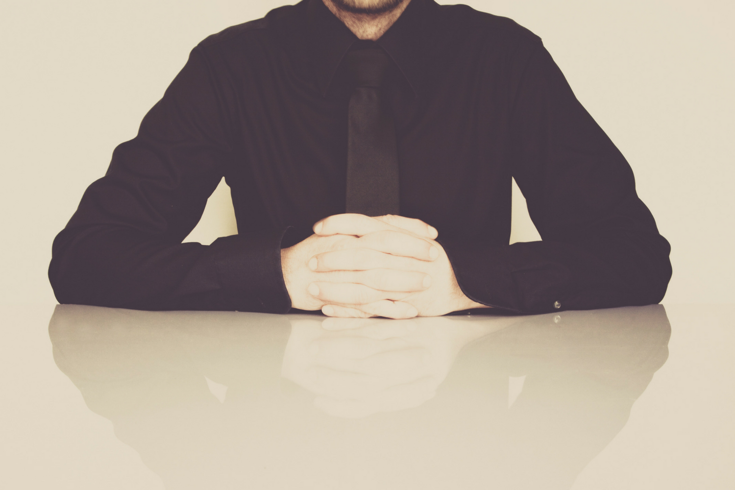 Business owner in a dark suit with hands clasped on a table, illustrating the difficulty of hiring good people, from Martin Holland, Anneal Business Coaching