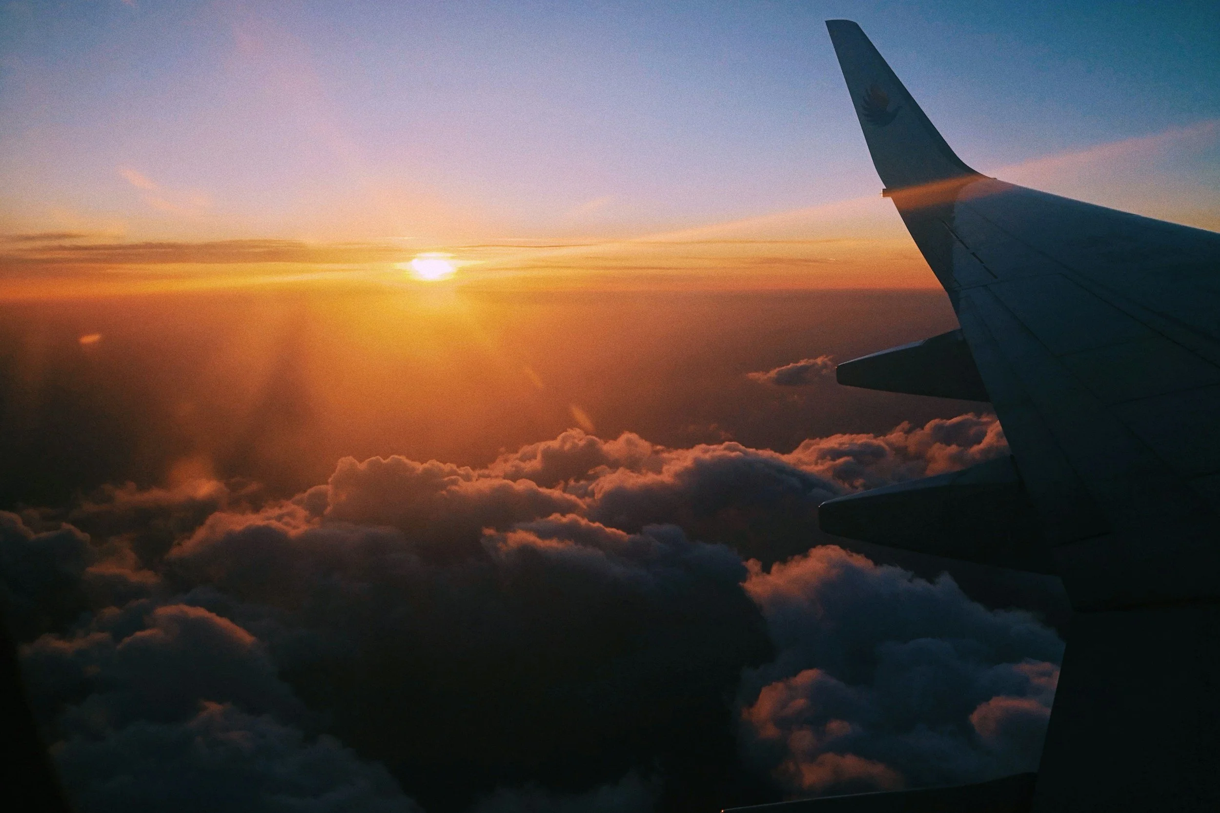 Photo taken from an airplane window showing a sunset above the clouds with the airplane wing on the right side.