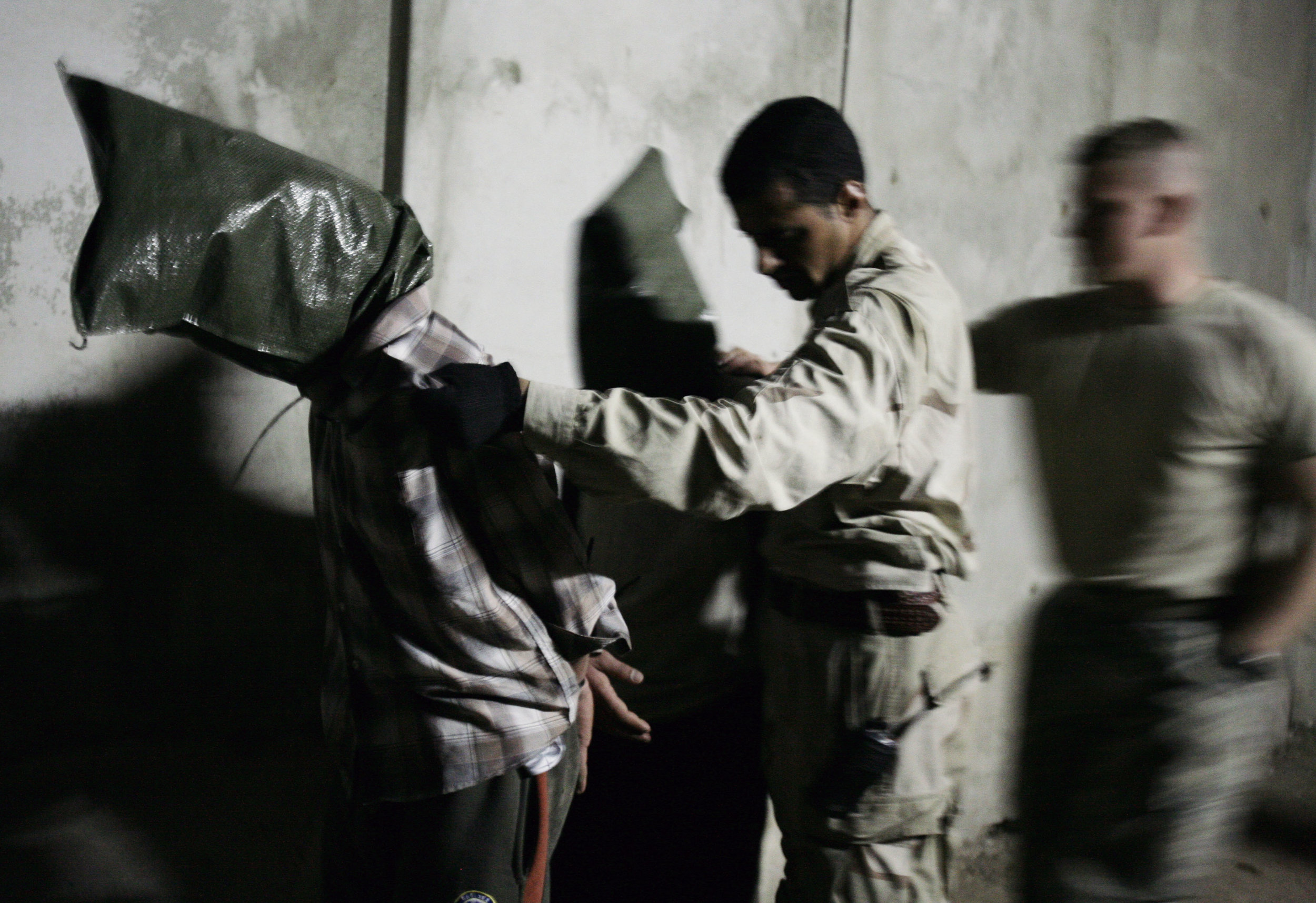A U.S. soldier, assists an Iraqi soldier with two men detained in a raid by Iraqi troops in Mosul on March 22, 2008.