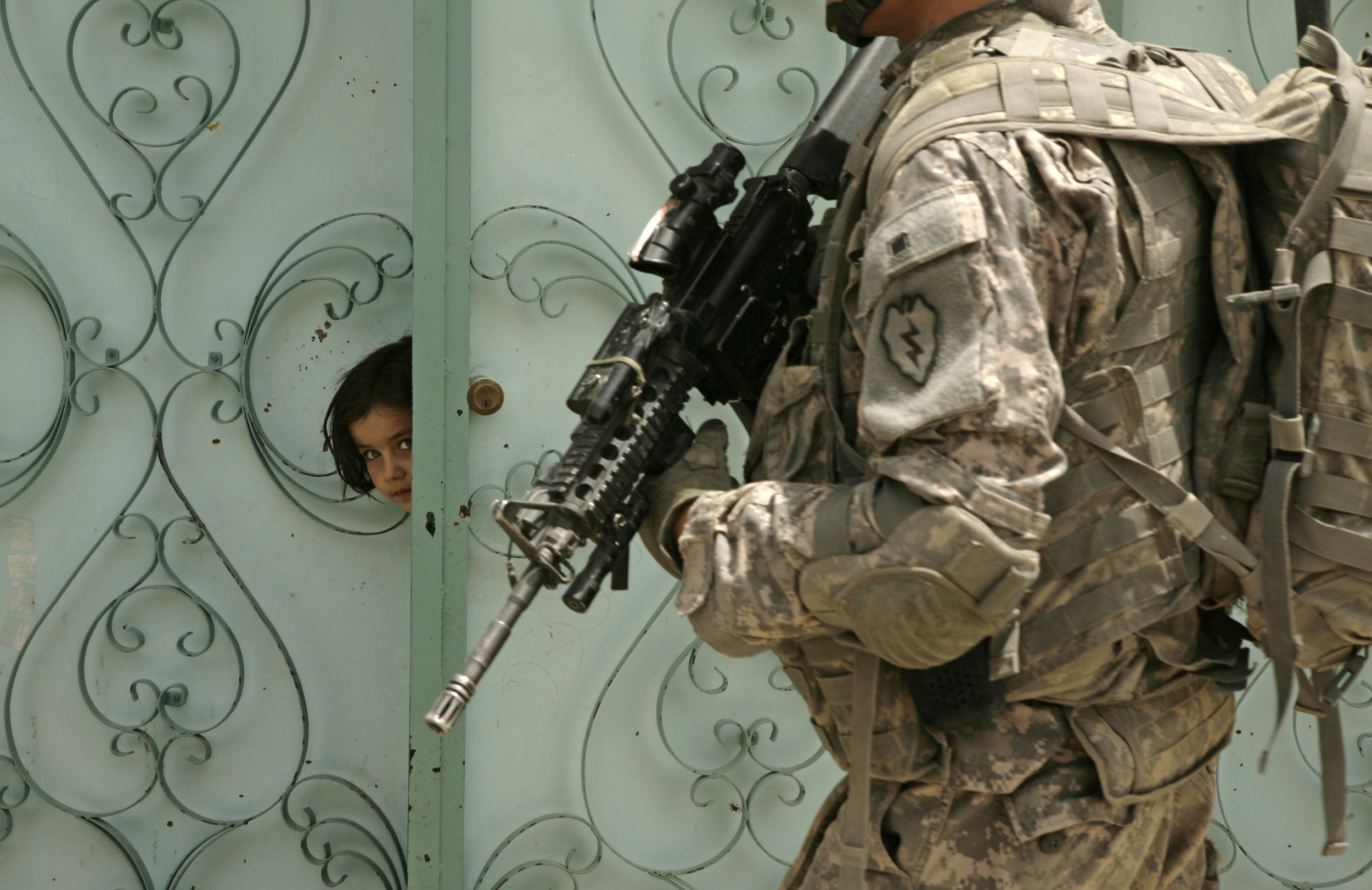 A girl peers from her front gate as a U.S. soldier patrols in Mosul on June 9, 2009.