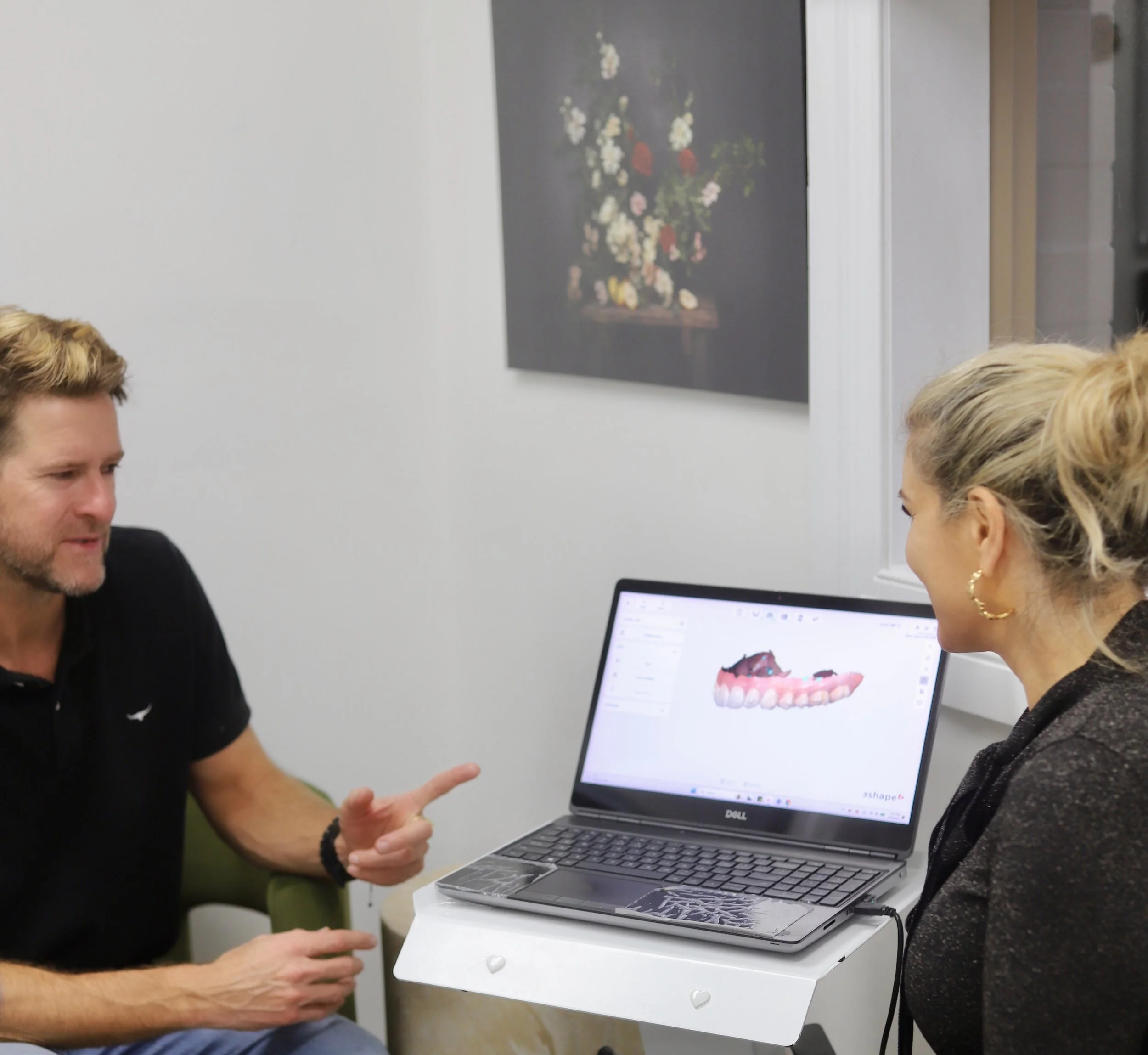 A man and a woman sitting across from each other discussing dental design on a laptop in a dental office.