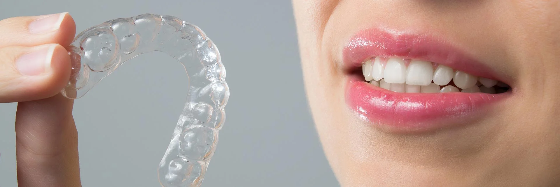 woman smiling holding her clear aligner for orthodontic treatment