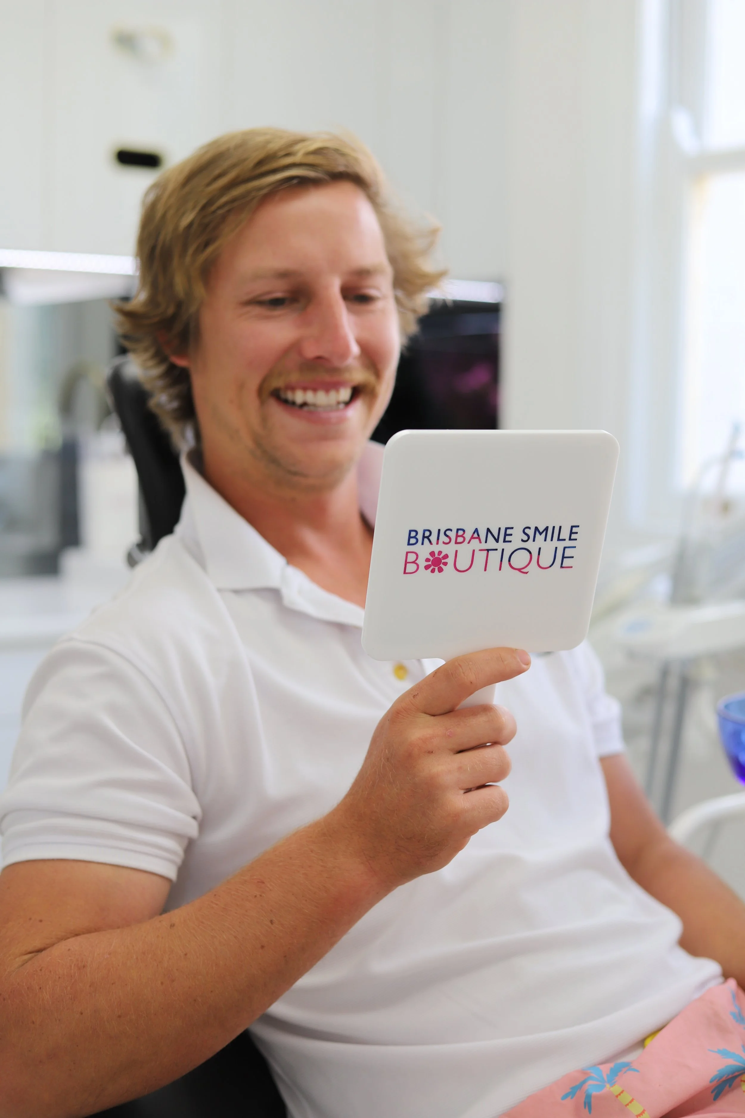 Young man looking at whitened smile in the mirror at the dentist