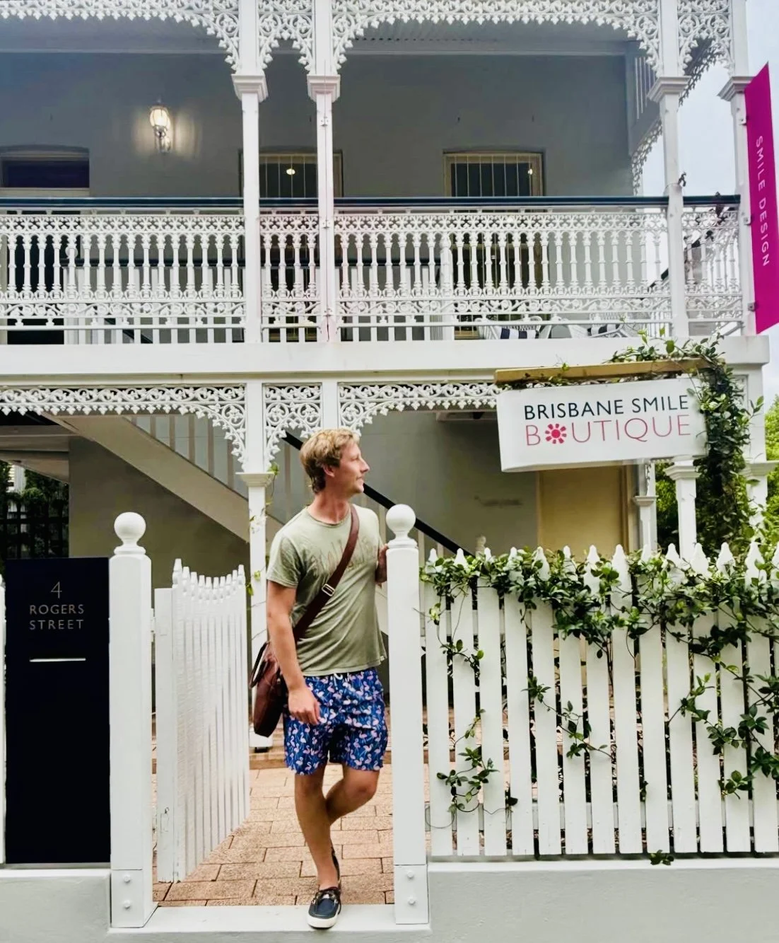 young man standing at the front fence of a heritage building in Spring Hill, Brisbane, after visiting a cosmetic dental clinic, looking at a sign that says Brisbane Smile Boutique