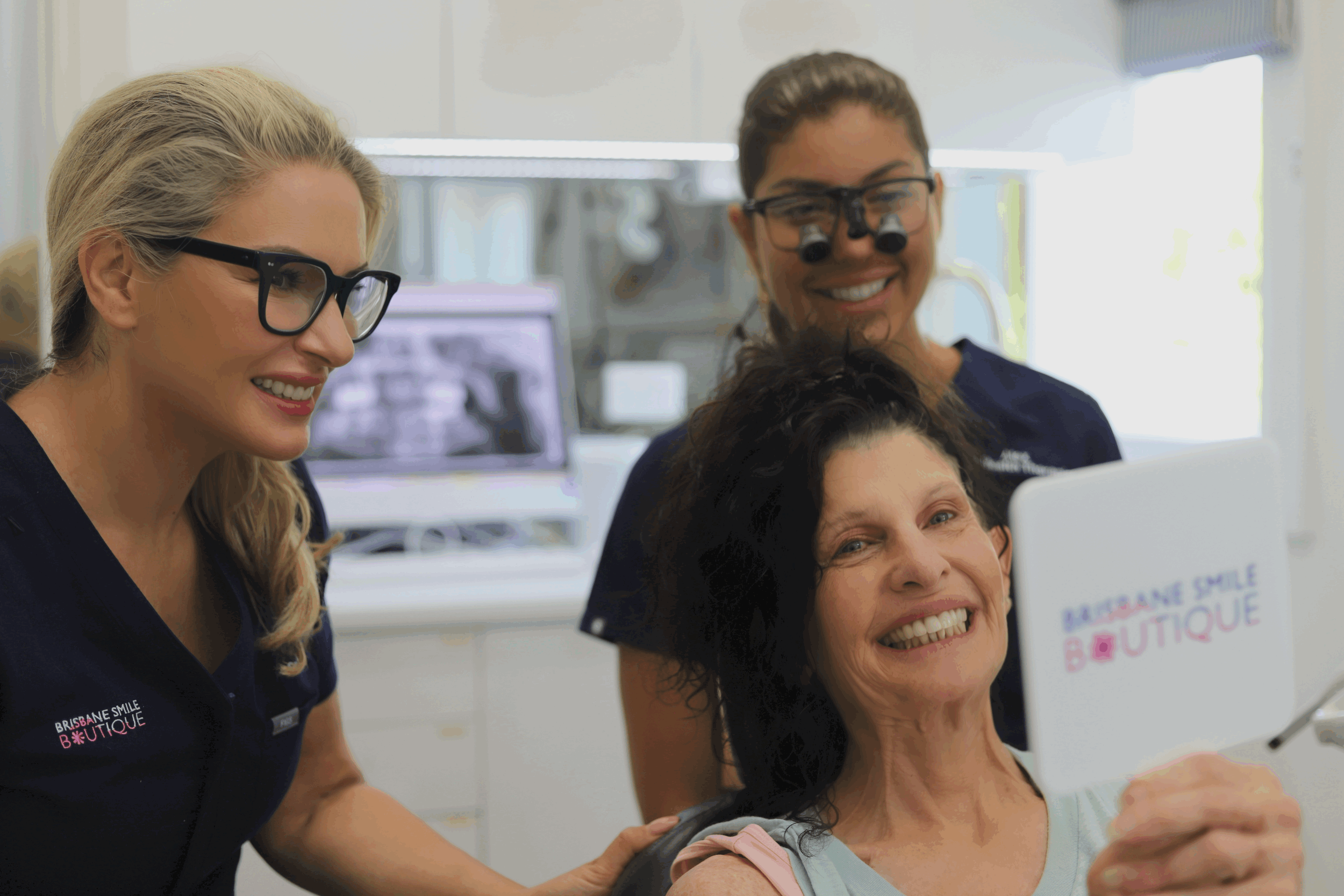female Dentist wearing scrubs at brisbane smile boutique with an elderly lady and an oral health therapist in the background