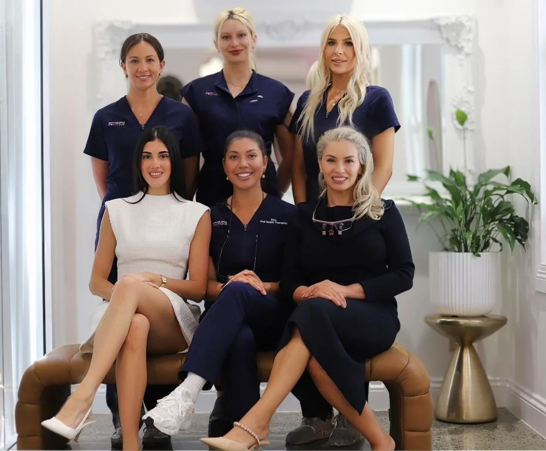 six female dental professionals at Brisbane Smile Boutique, some in scrubs looking at the camera in a dental office