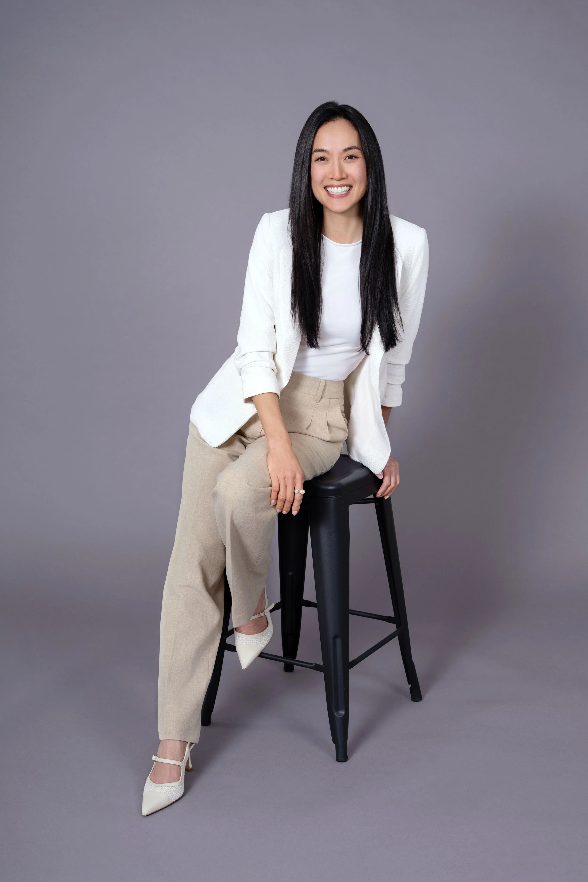 Female brunette Dentist, Dr Diane Nguyen, seated on a stool in a photo studio