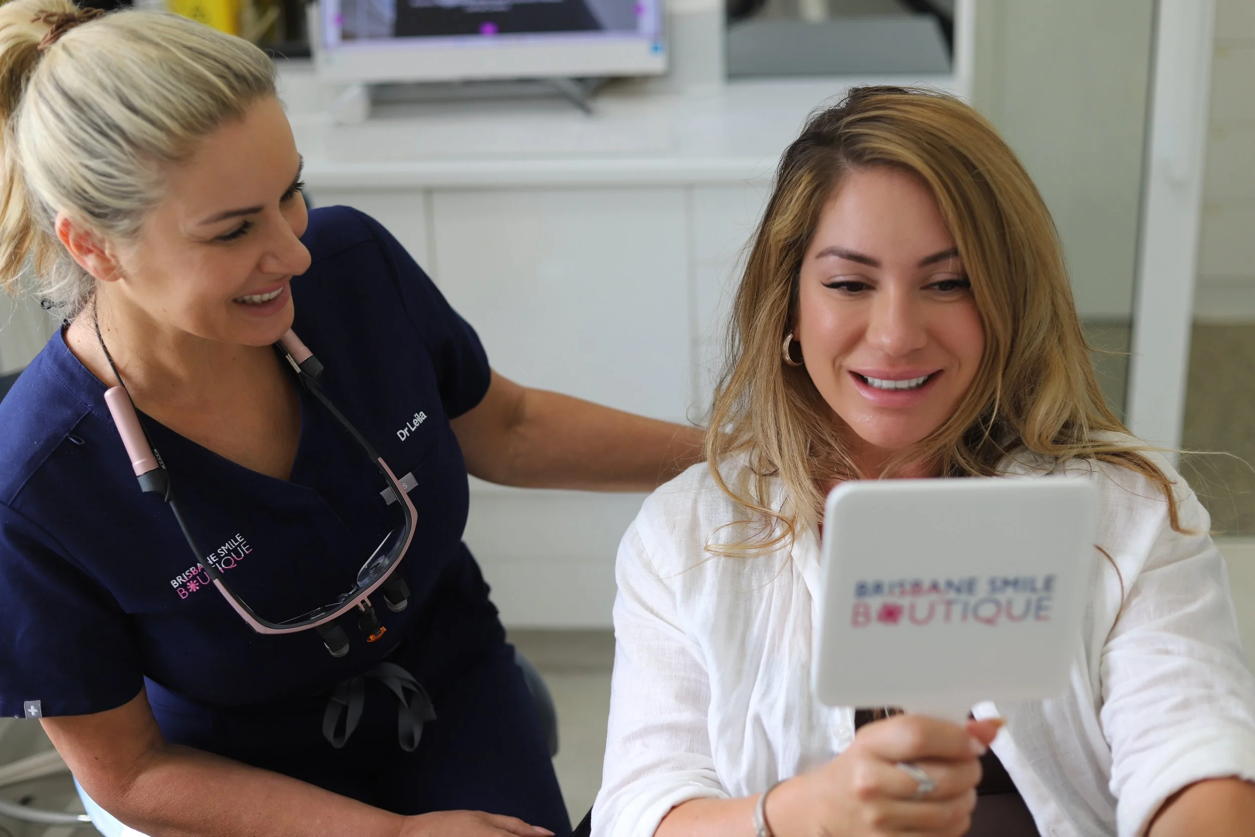 Female cosmetic dentist, Dr Leila haywood at Brisbane Smile Boutique Dentistry with a beautiful woman who is looking at her smile in the mirror