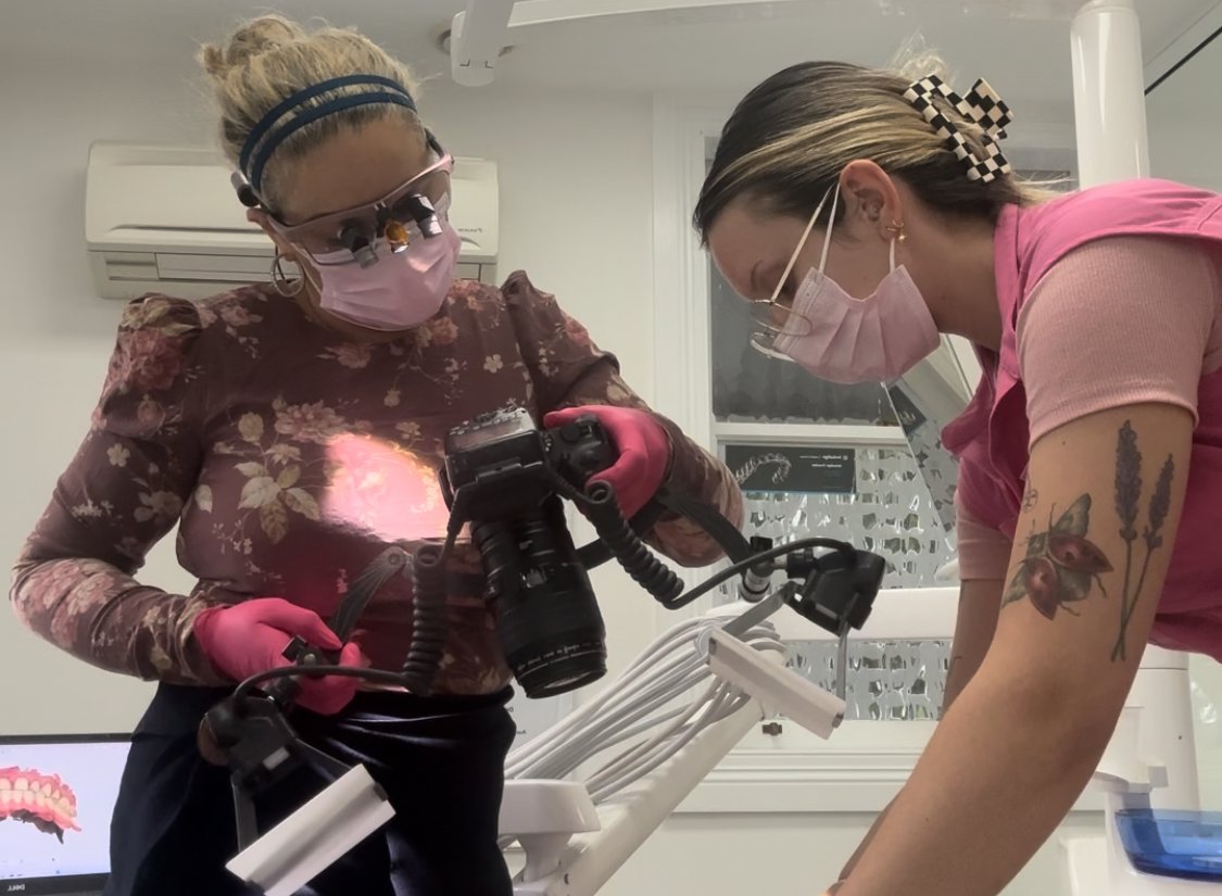 female dentist in a floral shirt with loupes on, taking an image of a patient, with an assistant helping, at brisbane smile boutique, an all female aesthetic dental clinic in Spring Hill. 