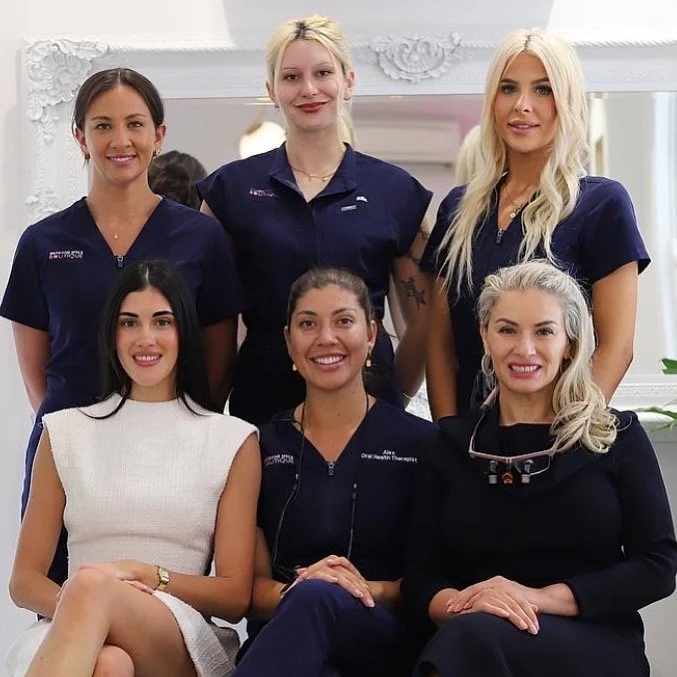 Six female dental professionals smiling at the camera at Brisbane Smile Boutique Cosmetic dentistry in Spring Hill, Brisbane, a team of female dental professionals providing cosmetic dentistry, porcelain veneers, smile makeovers and Invisalign