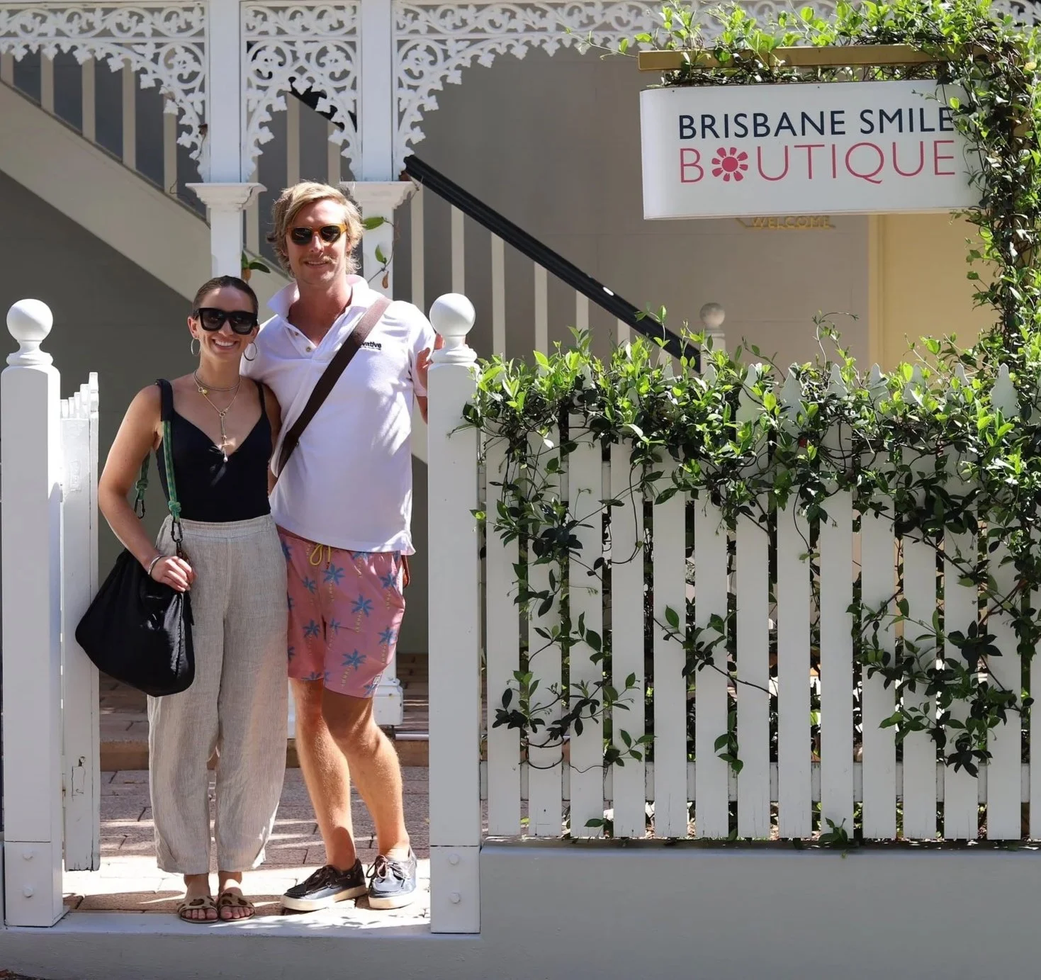 a young couple standing at a gate with a white picket fence in front of a dental surgery in a house called Brisbane Smile Boutique