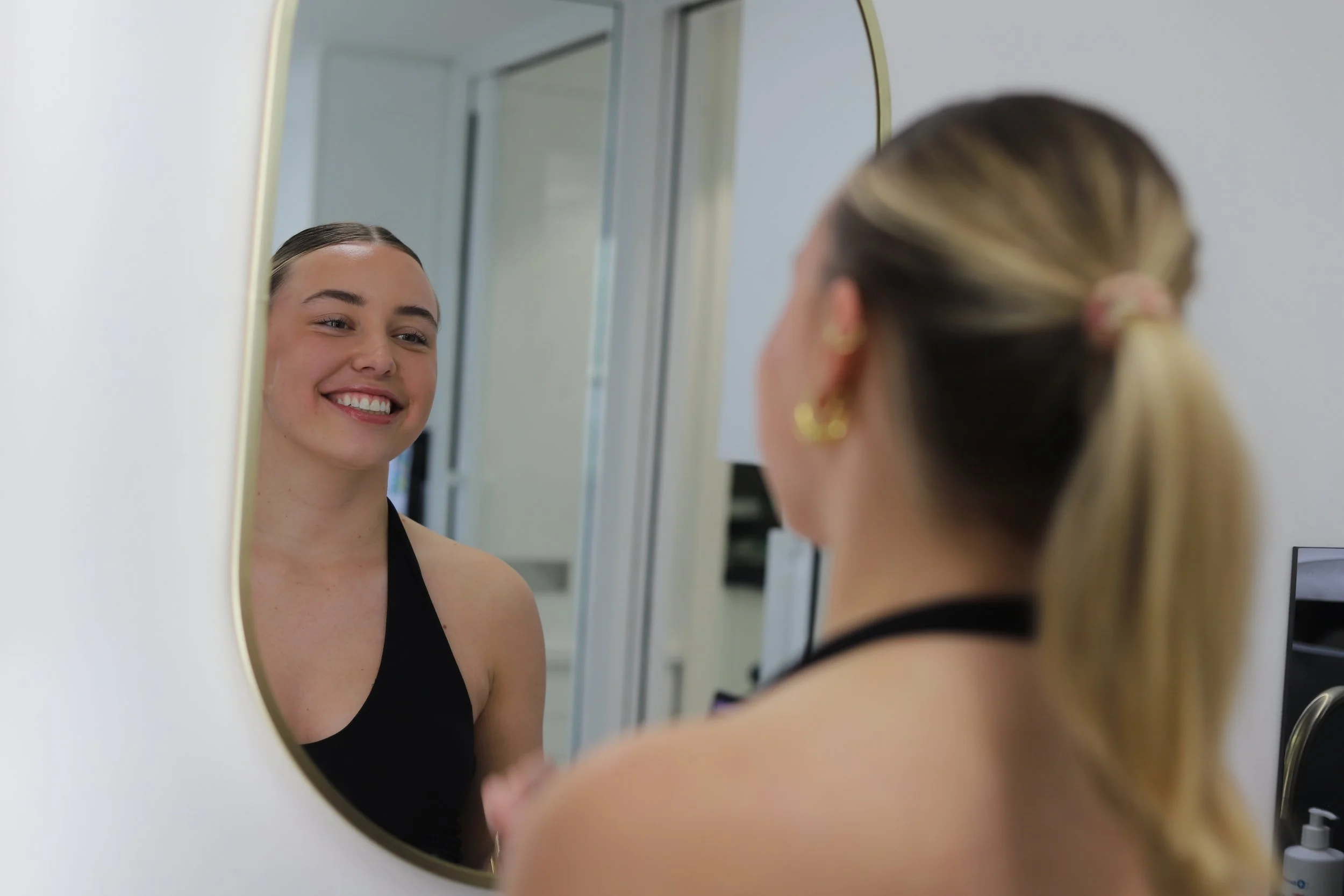 Attractive female dental patient looking in the mirror at her smile.
