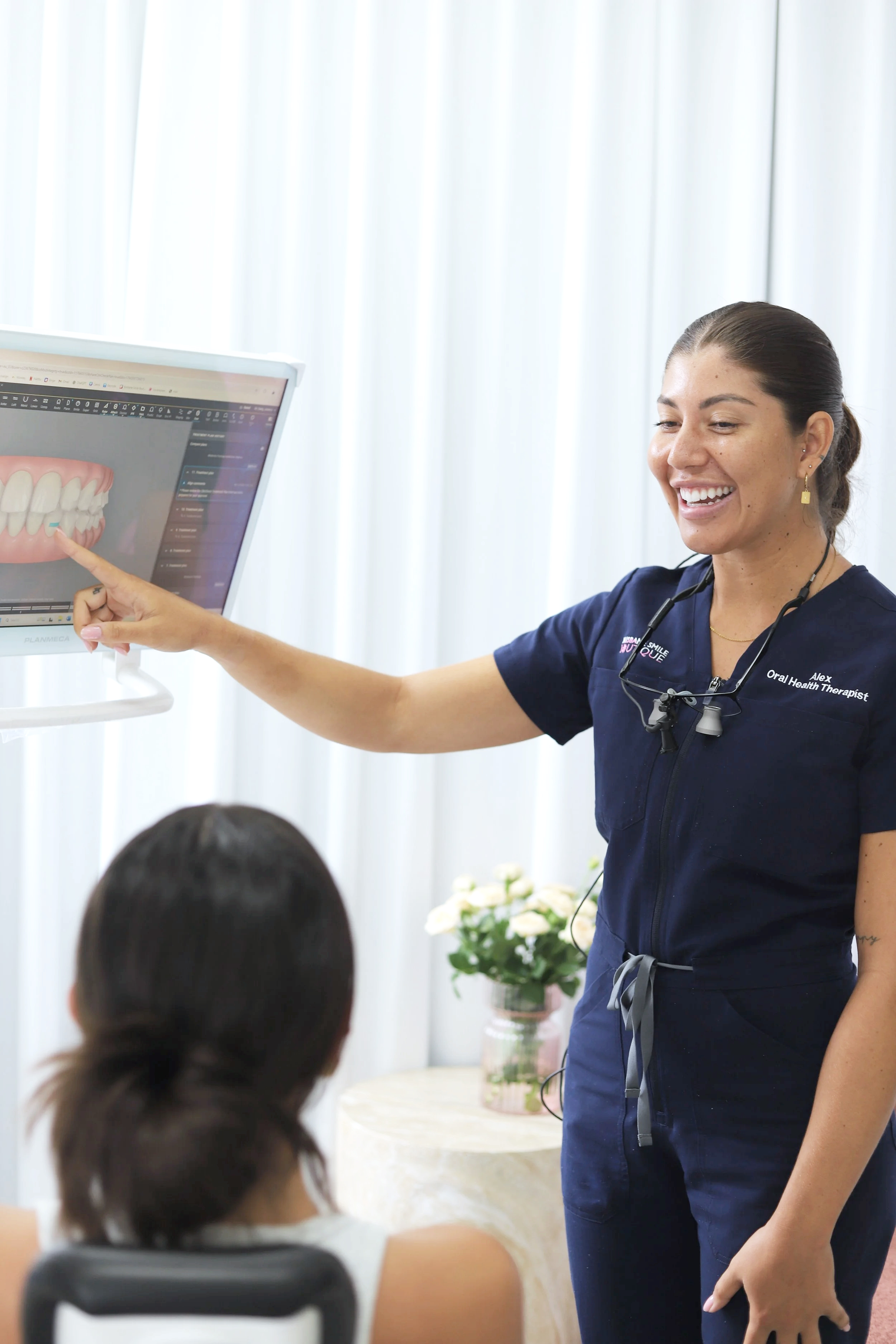 Female dental professional, oral health therapist, Alexandra Forbes smiling at invisalign portal with female patient in chair at Brisbane Smile Boutique Aesthetic Dental Clinic in Spring Hill, Brisbane, Queensland, Australia