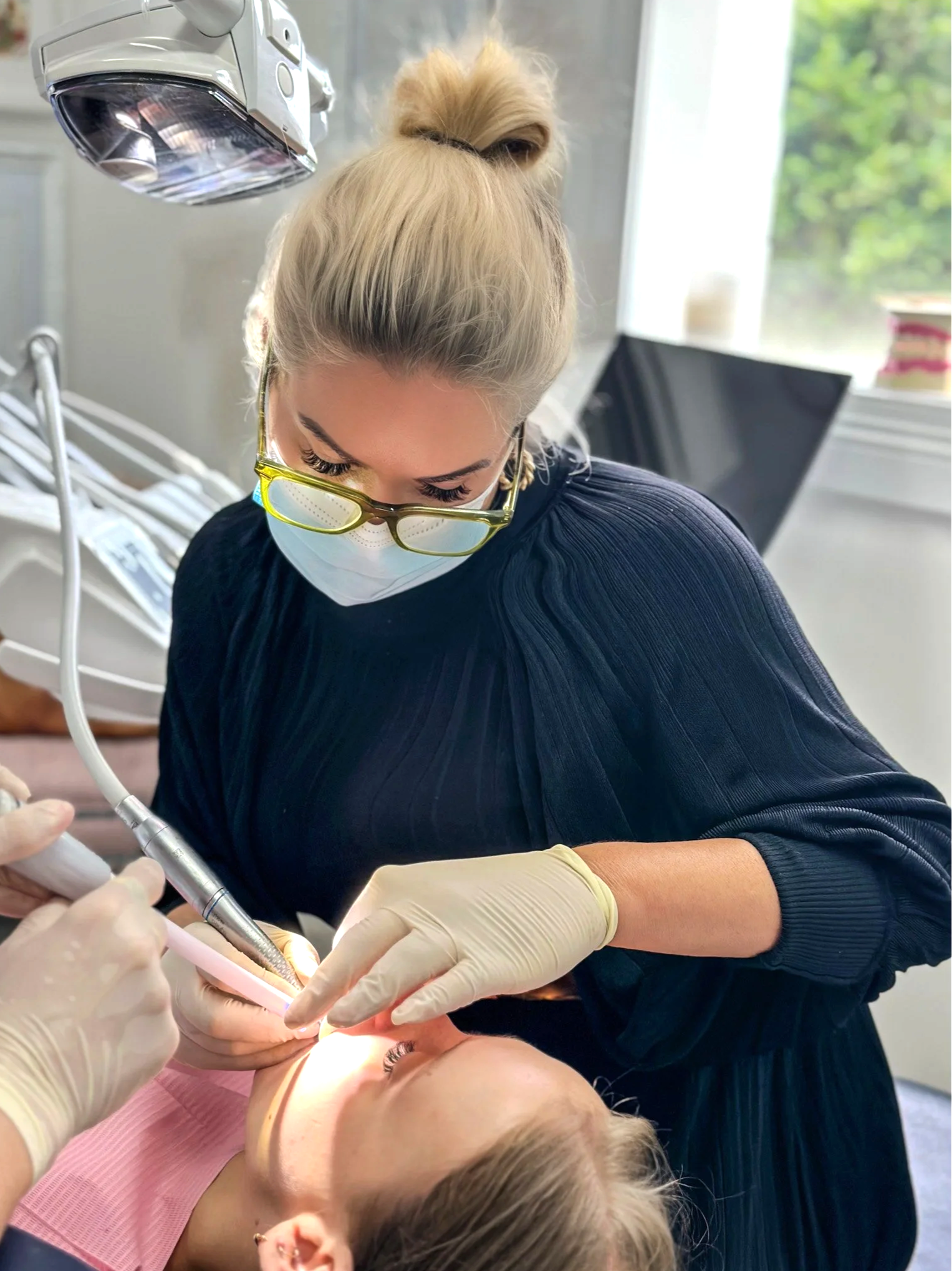 female dentist at Brisbane Smile Boutique with mask, gloves and glasses on and black dress, working on a female patient