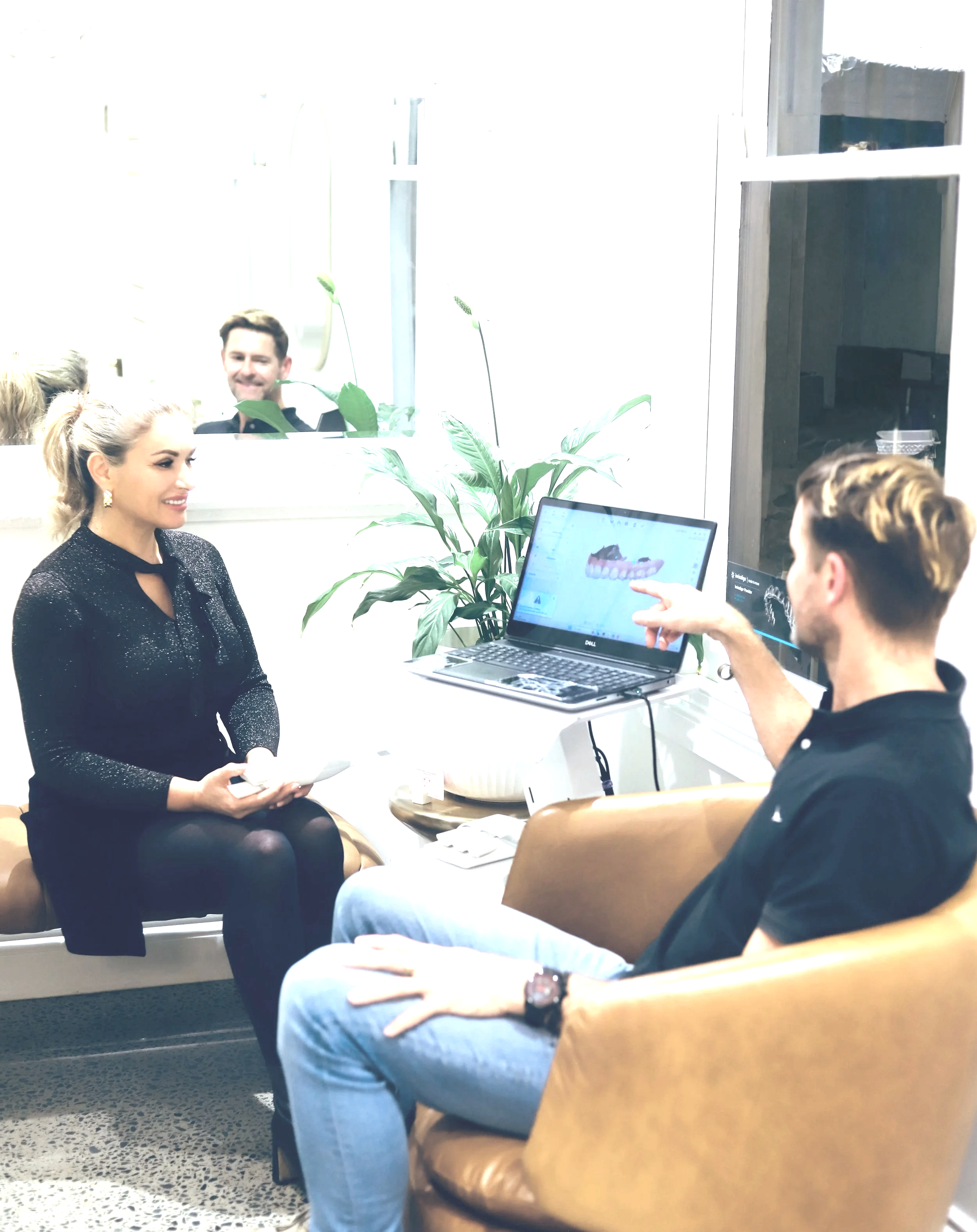 A dental consultation at Brisbane Smile Boutique where a dentist is explaining dental model to a woman patient, with a man observing and pointing at a computer screen, in a well-lit dental office.