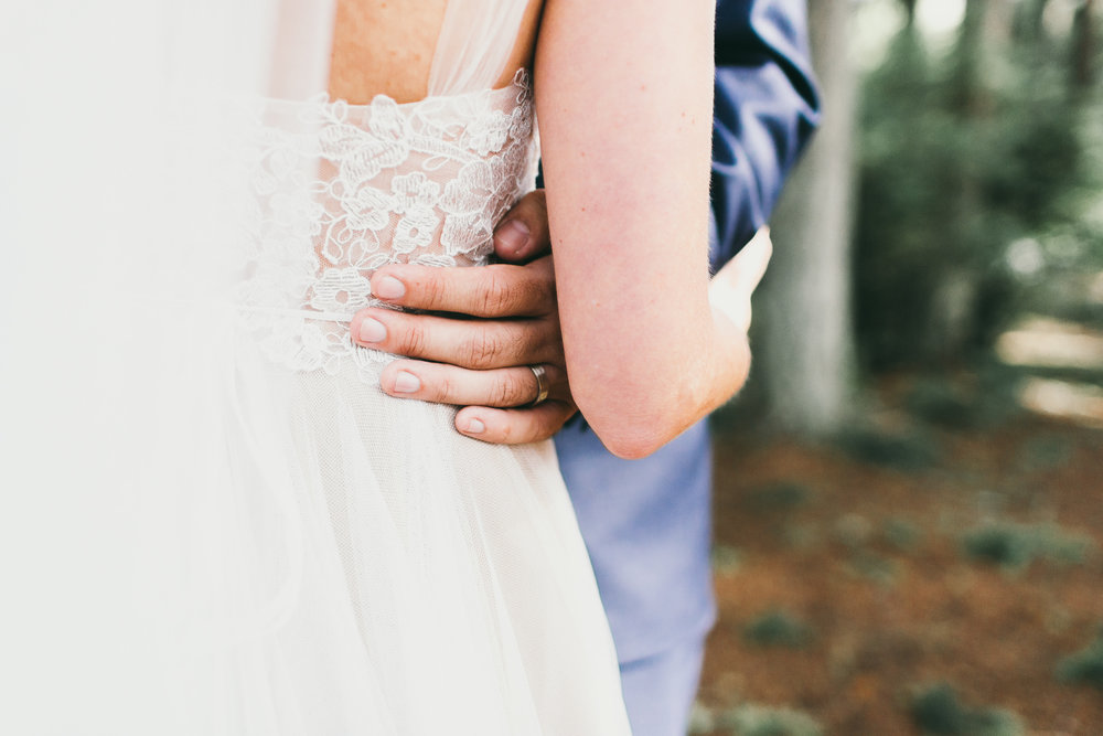 groom tenderly holds bride's waist in forest
