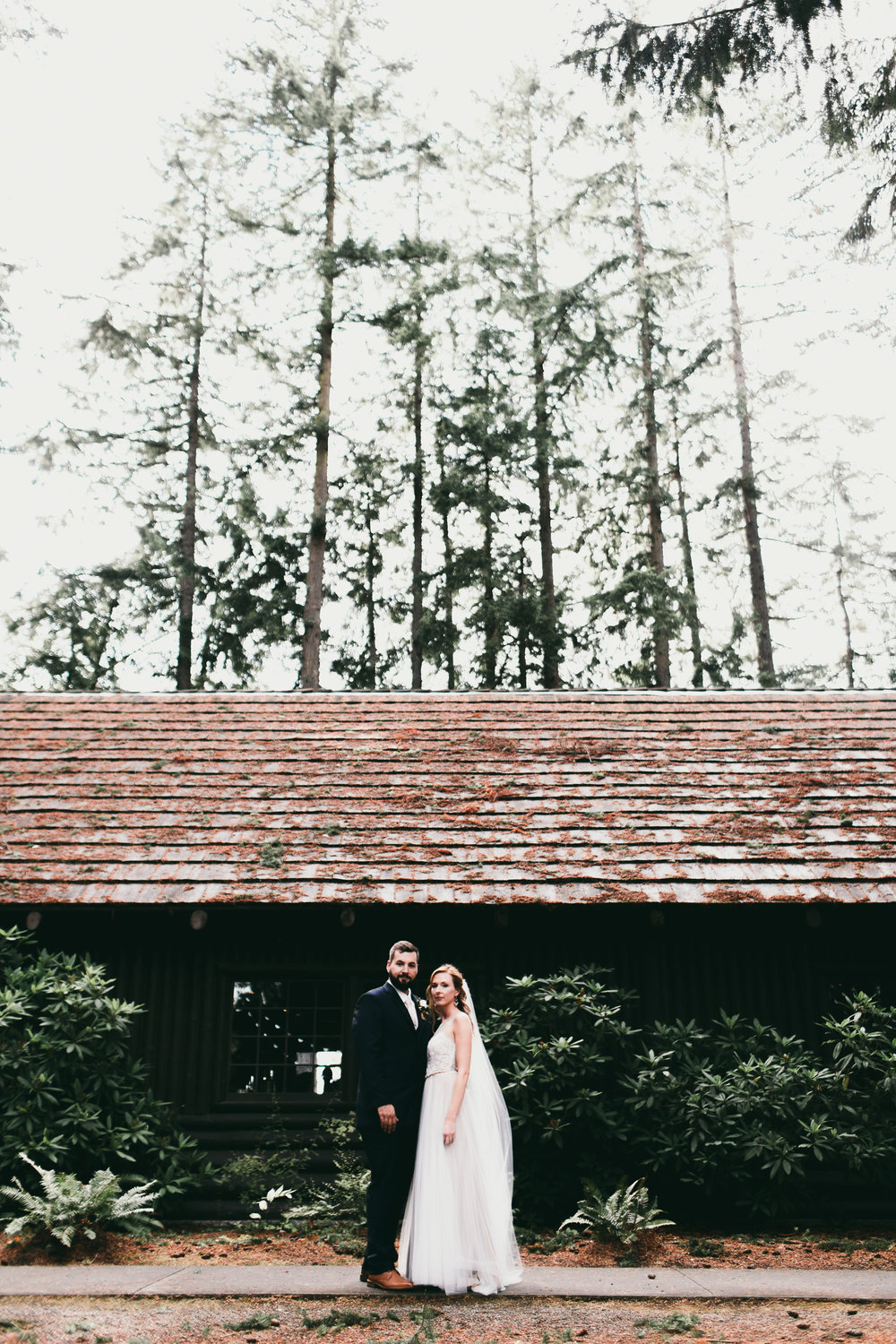 bride and groom in front of log hall at kitsap memorial state park