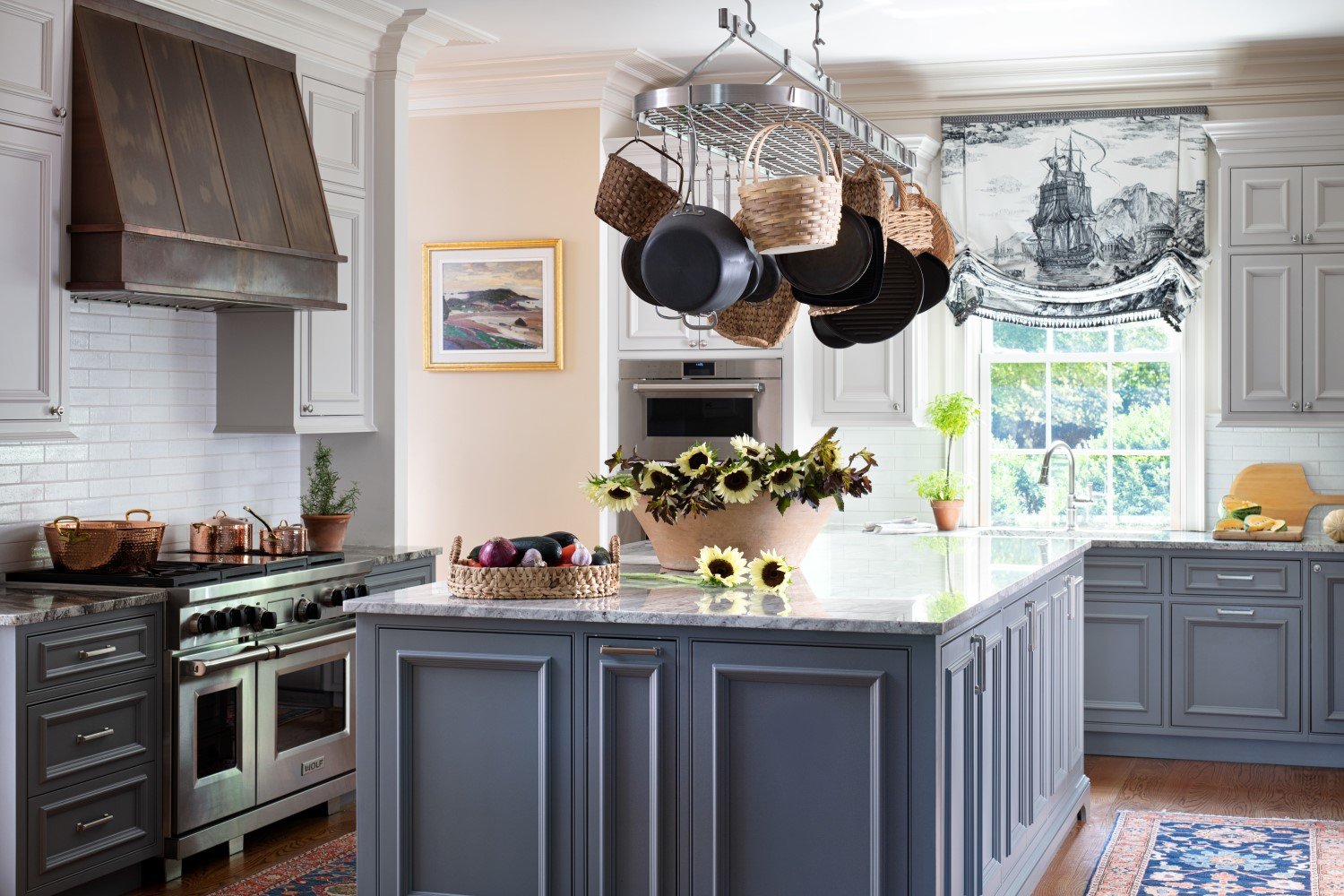 This kitchen by Bridget Beari Designs has a classic French feel with the antiqued range hood, the central pot rack hung with baskets and pans, and the rich blue on the cabinetry 