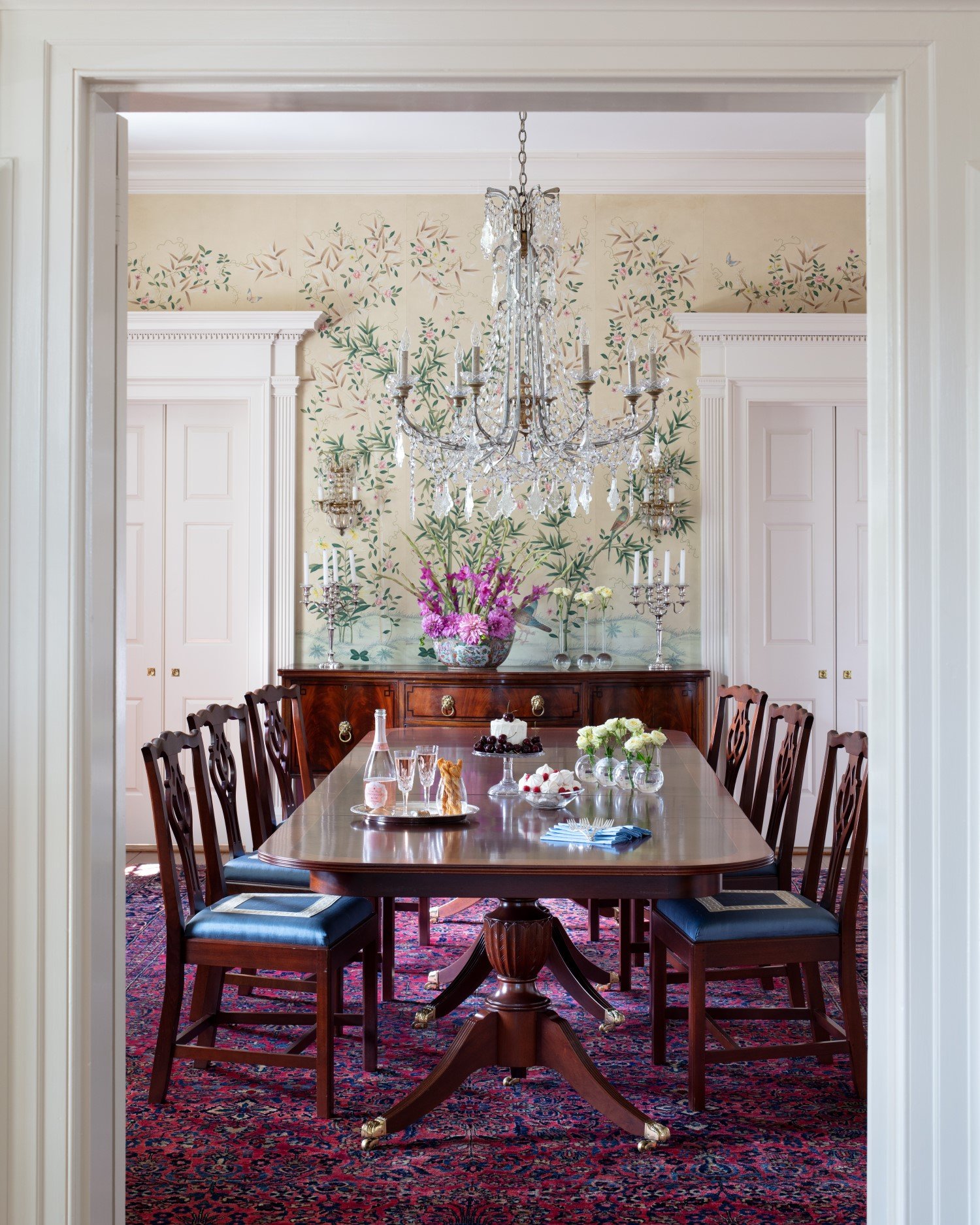  Formal dining room with classically designed furniture, an ornate crystal chandelier, and nature-inspired wallpaper by Bridget Beari Designs 