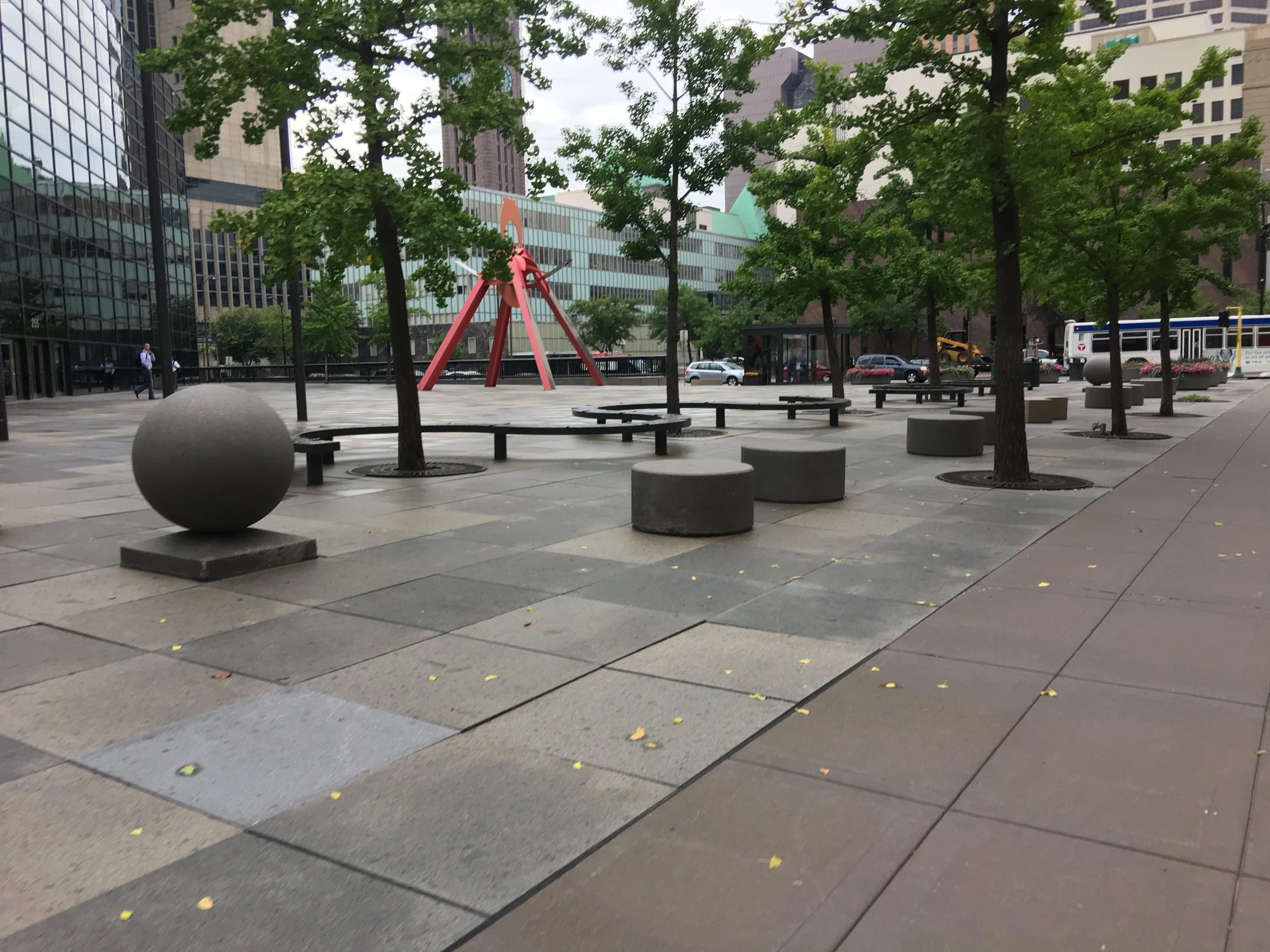 Plaza in Minneapolis with seating, artwork, trees, and hardscape, but no visitors.