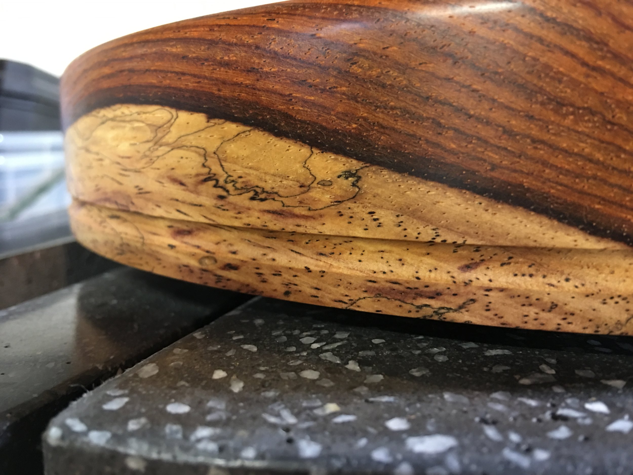 Here you can see the sapwood of the Cocobolo, which has a drastically different color than the deep red-orange heartwood. This is set atop the black plinth, which has its white aggregate exposed to create an almost stone-like texture. A groove is cut into the platter to keep the belt in place. 
