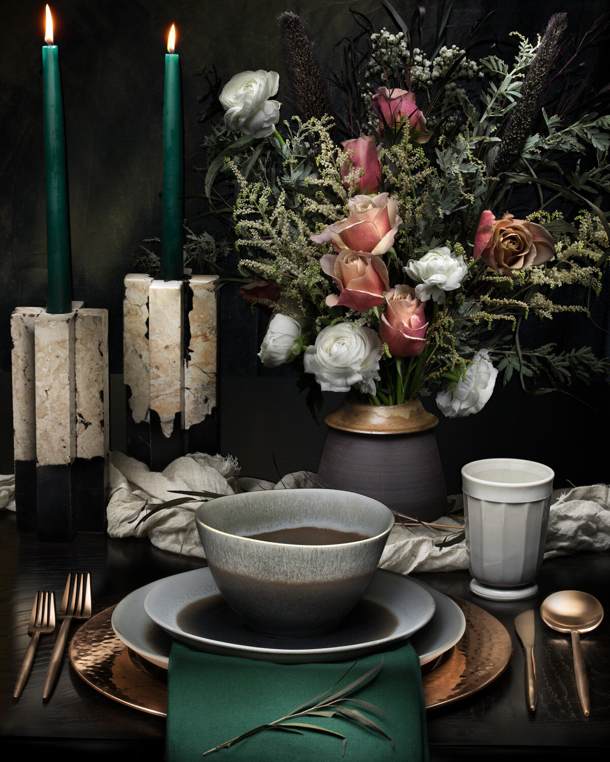 A moody dining table setting with deep green candles, soft florals, and elegant dinnerware. Home decor photography by Nightflare Creative.