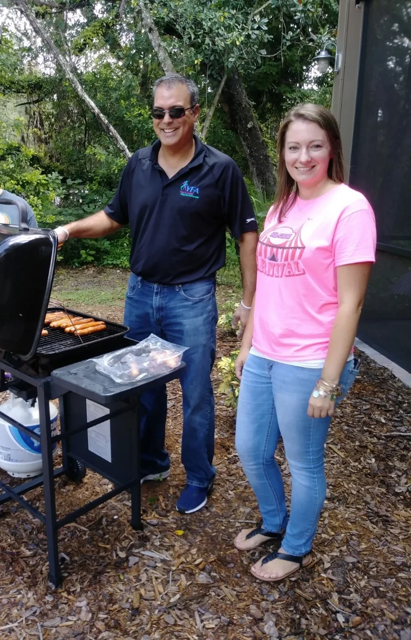 Prepping barbecue treats for the RAP House Back-to-School Carnival. Left to right: Grillmaster Keith Mukherjee, VP of Central Programs, grilling hot-dogs, and standing beside him is Cayse Houston, RAP House Program Director. This was an opportunity for RAP House temporary resident youth and staff to commingle on the lovely grounds of the shelter before the start of a new school year in Pasco County.