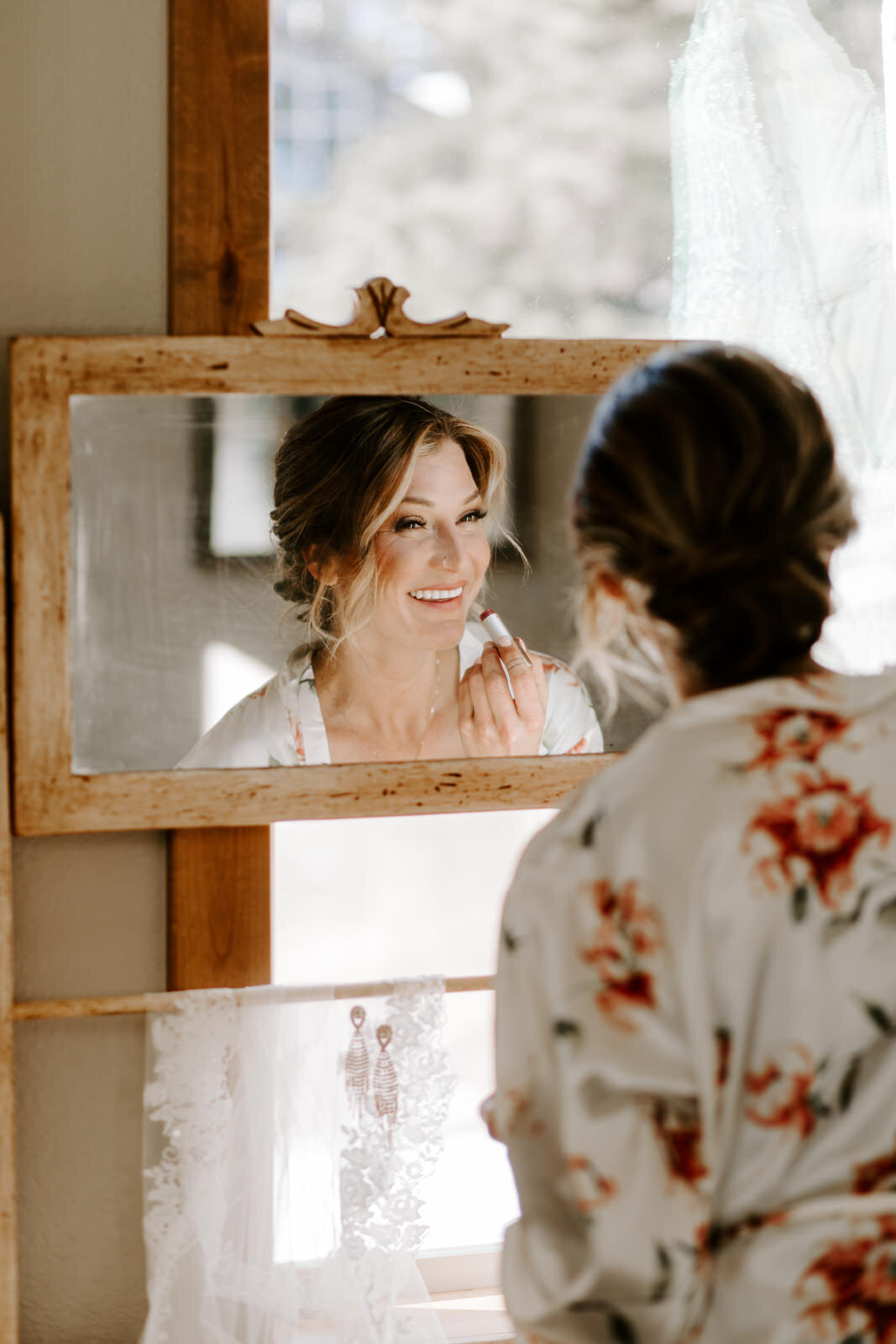 bride getting ready and putting on lipstick at antique dresser at Estes Park AirBnB Elopement for an LGBTQ couple with Colorado elopement photographer Diana Coulter