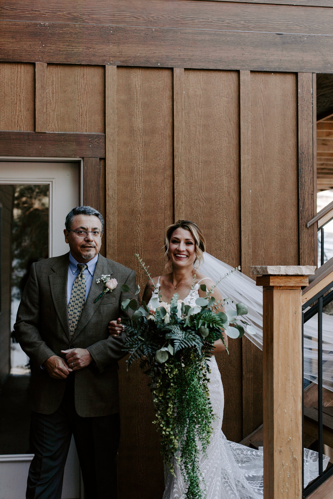 dad walking his bride down the aisle and while she holds her bouquet and smiles at the camera at Estes Park AirBnB Elopement for an LGBTQ couple with Colorado elopement photographer Diana Coulter