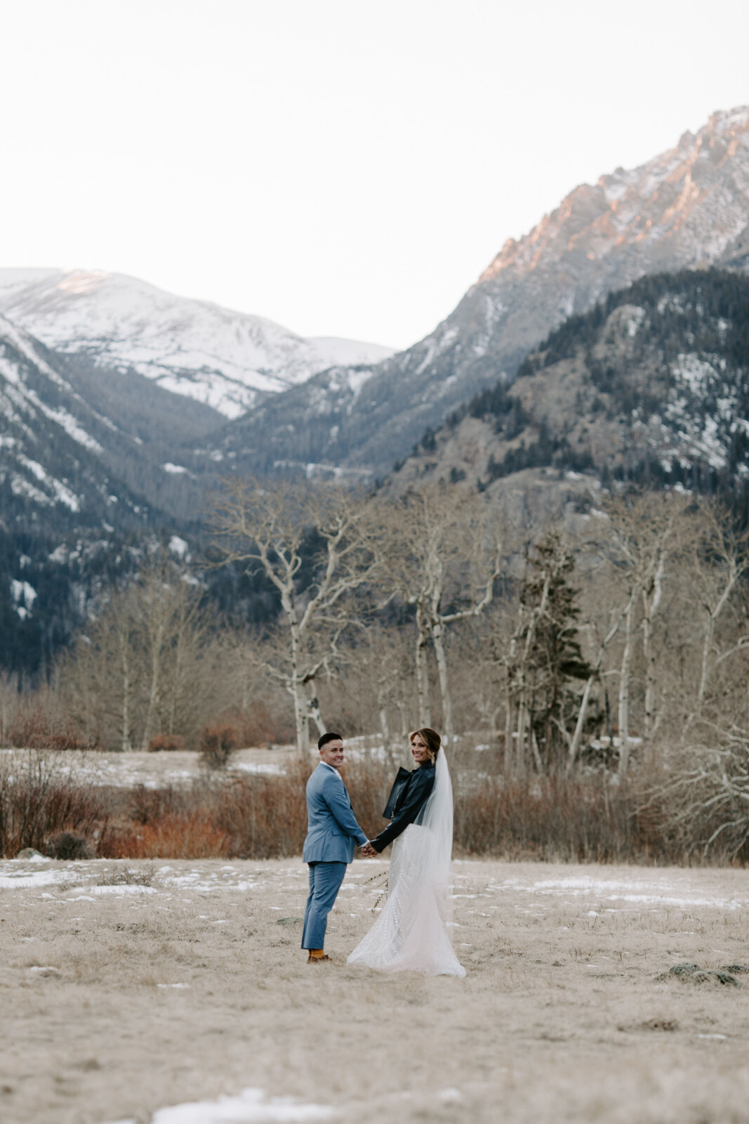 LQBTQ couple holding hands and looking at the camera during winter elopement in Rocky Mountain National Park in Colorado at sunset with wedding photographer Diana Coulter