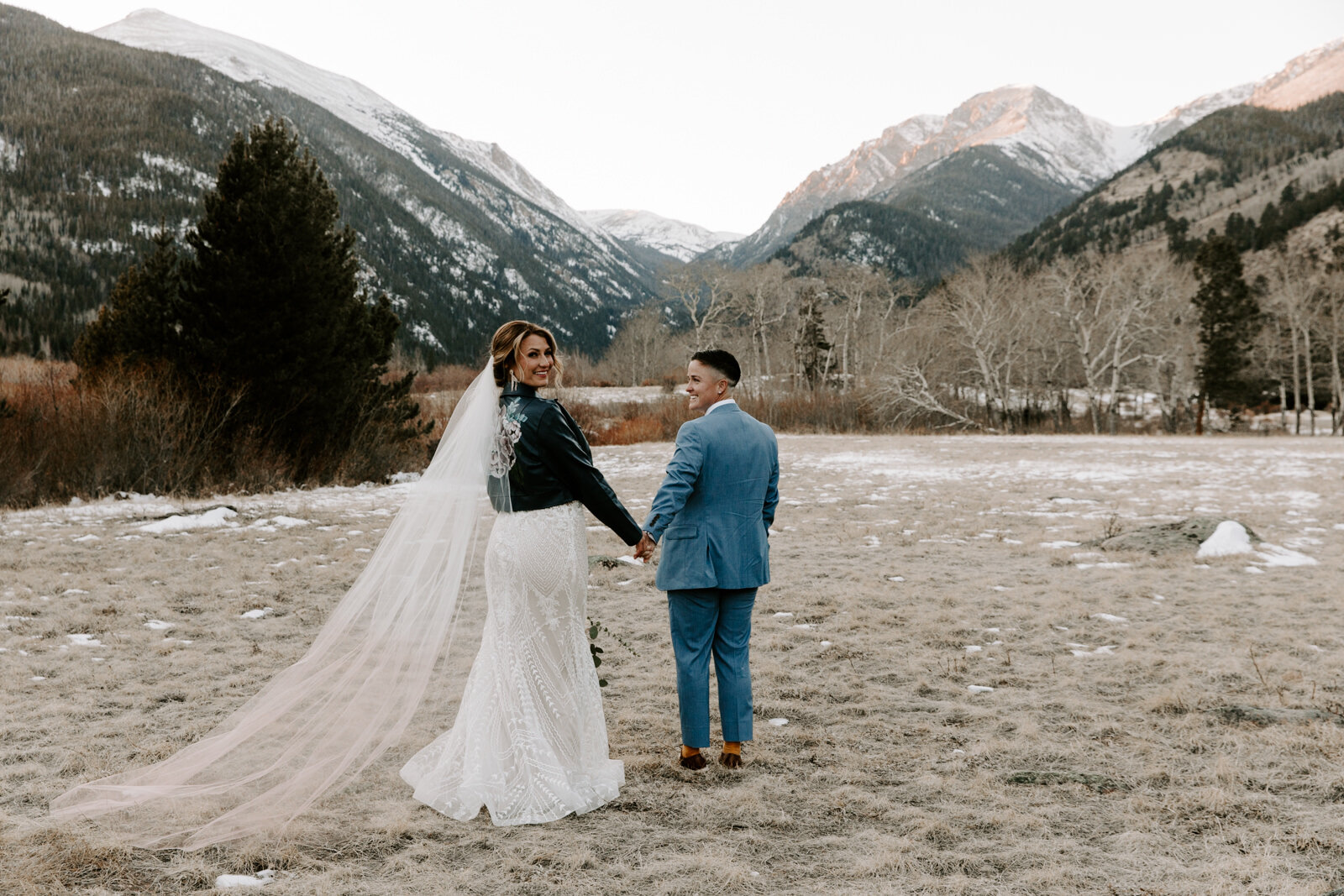 bride in her cathedral veil and black leather jacket looking at me and broom wearing a blue suit looking at the bride during winter elopement in Rocky Mountain National Park in Colorado at sunset with wedding photographer Diana Coulter