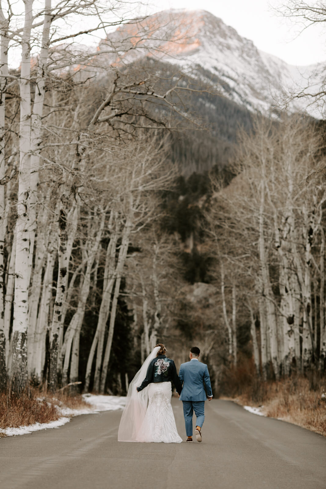 playful LGBTQ couple running towards the mountains on a roach with aspen trees in the background in Rocky Mountain National Park during winter elopement in Colorado at sunset with wedding photographer Diana Coulter