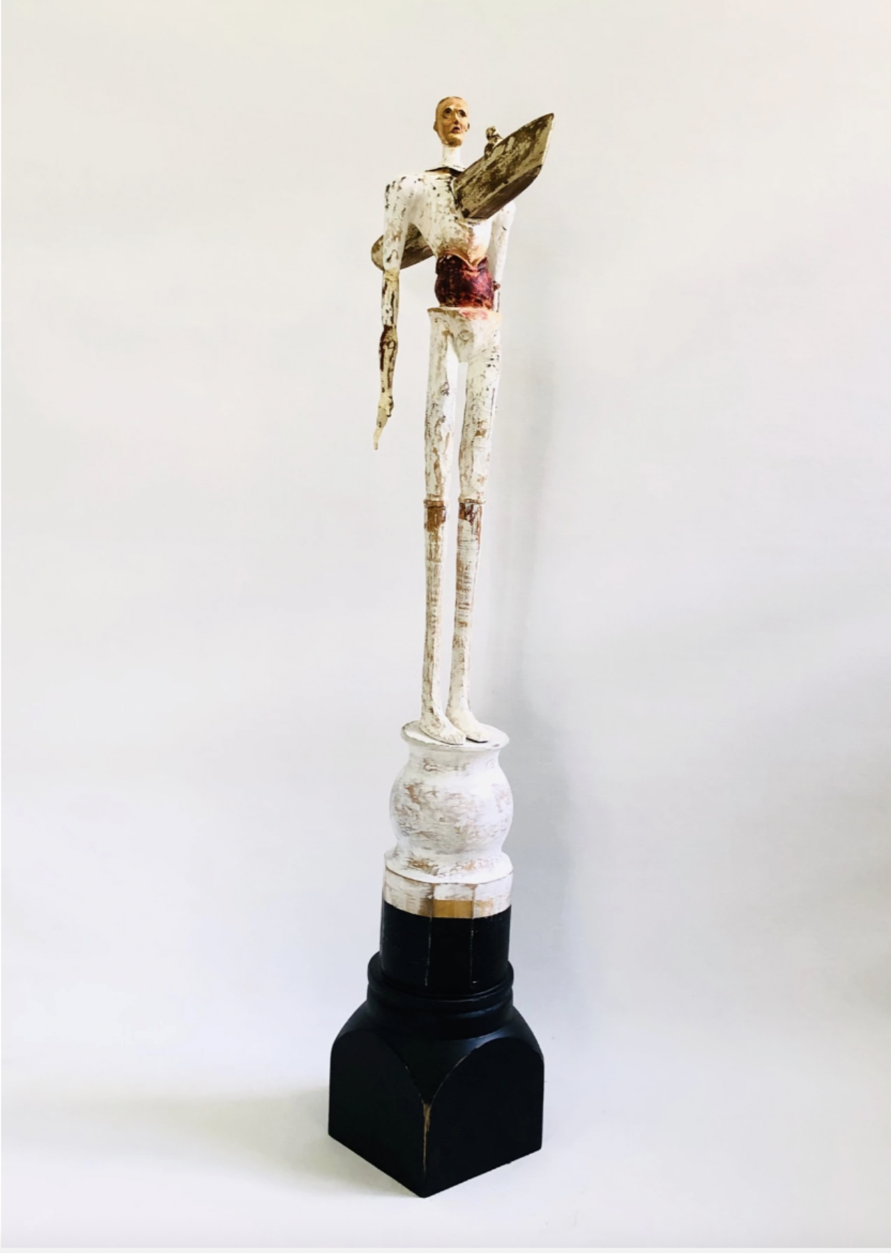An image of a sculpture titled Feeling Without Belonging by Cuban artist Ernesto Capdevila, represented by Conde Contemporary, featuring a wood carving of a tall thin man with a canoe coming through his chest.