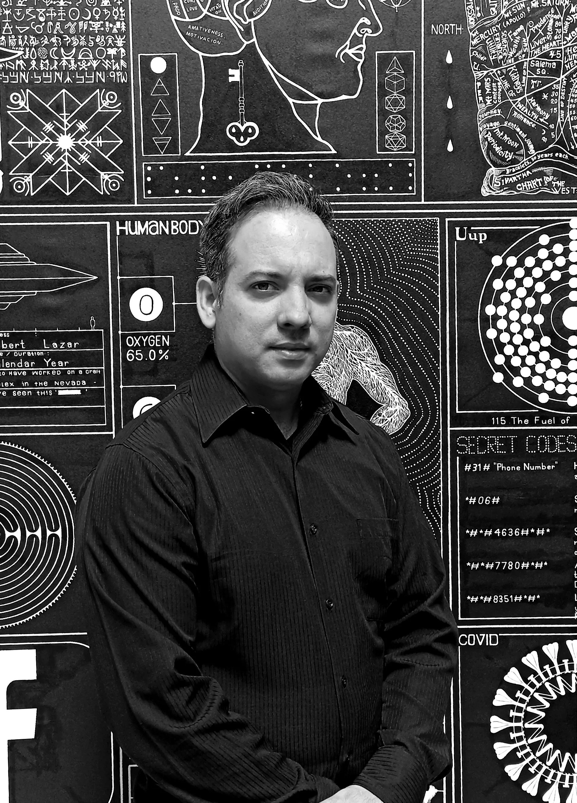 A photograph in black and white of contemporary Cuban painter, living in Mexico, Henry Rodríguez Bienes, standing in front of one of his paintings from the Criptograma series, available at Conde Contemporary.