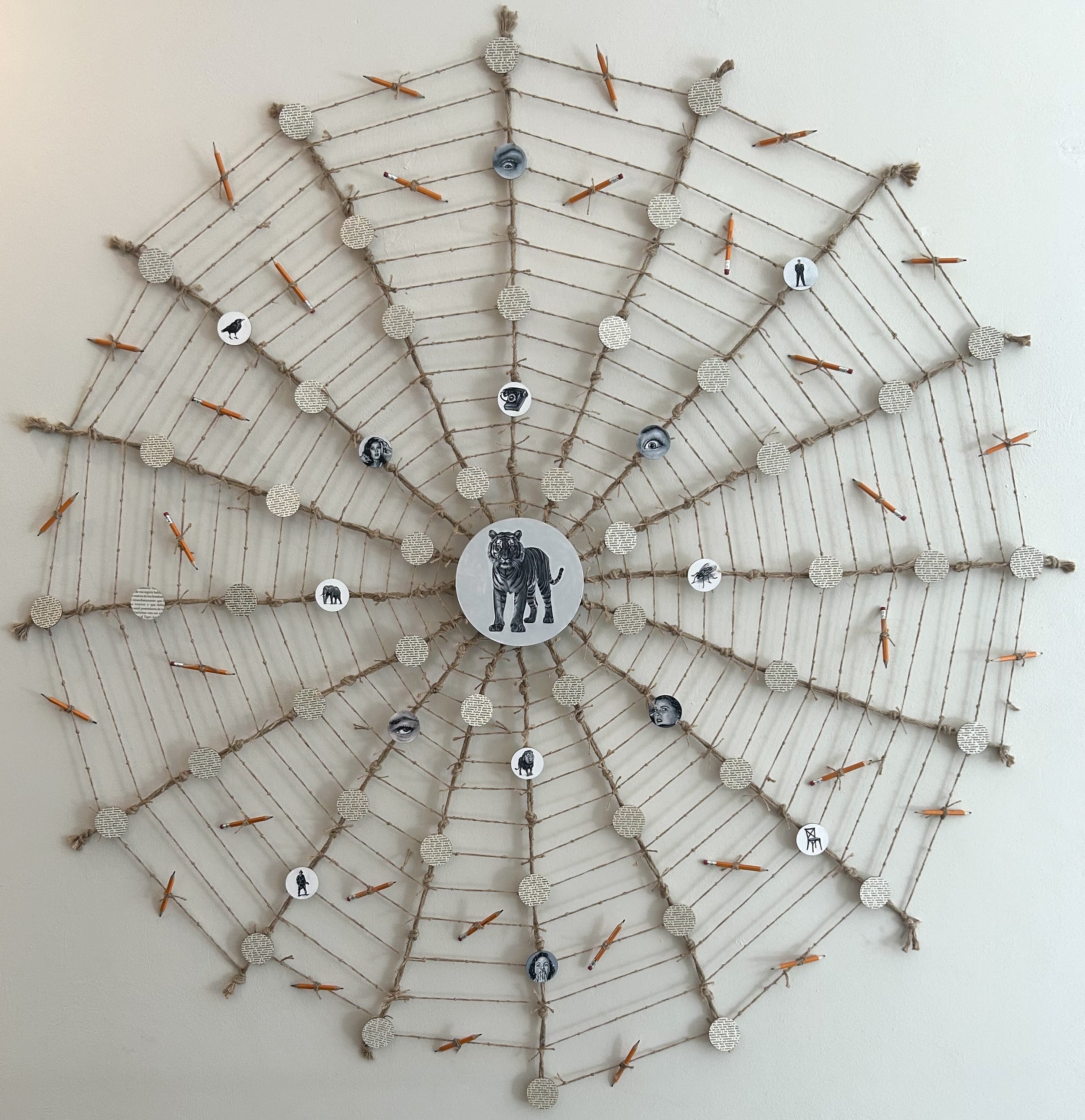 A mixed media artwork of a tiger painted on a central wooden circle at the middle of a jute web, surrounded by paper circles, pencils and small circular paintings, titled Tres Tristes Tigres, by Ruben Torres Llorca for Conde Contemporary.