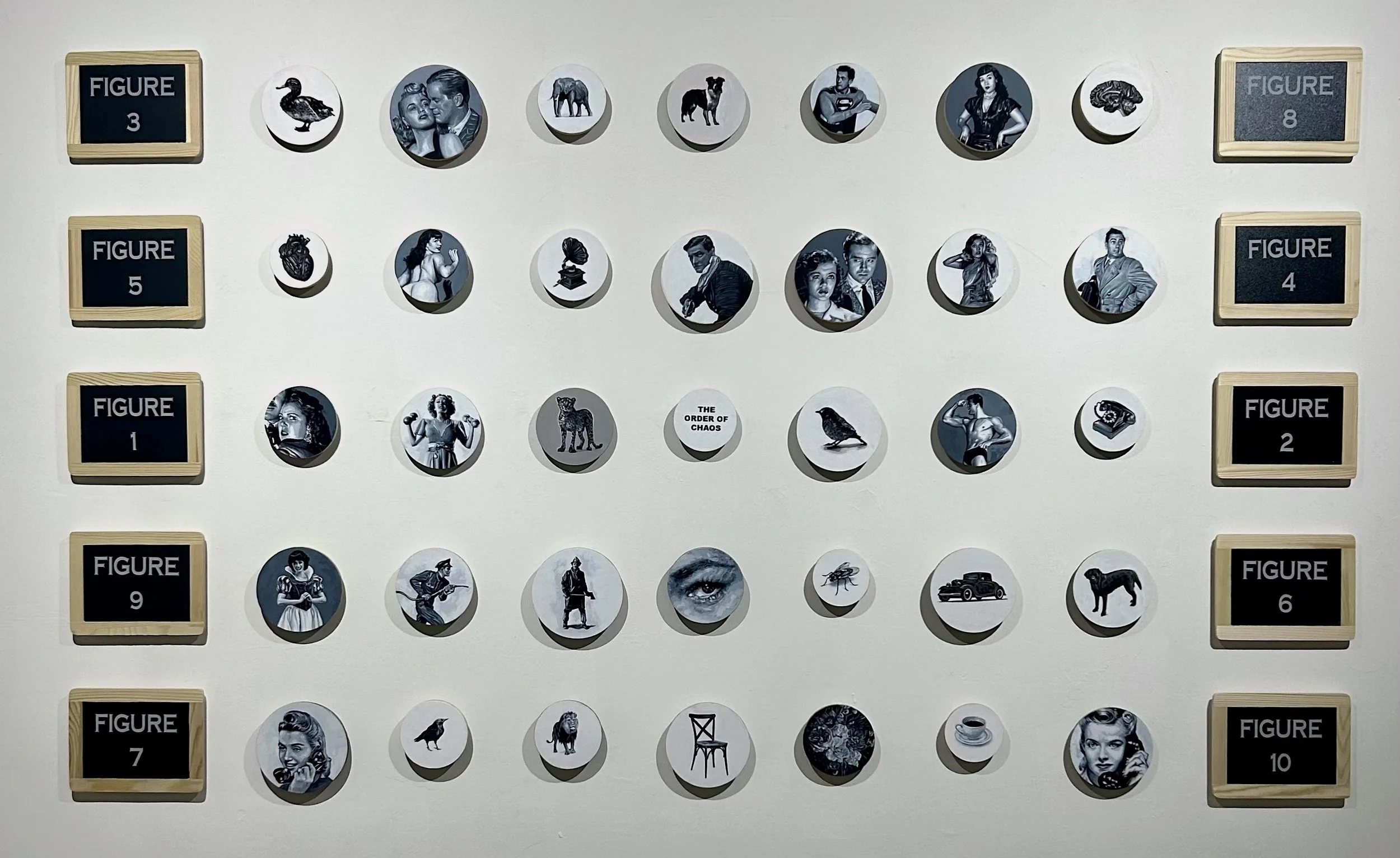 A mixed media artwork by Cuban conceptual artist Rubén Torres Llorca featuring 35 wooden rounds of different sizes painted in grayscale, subjects include women, snow white, a human heart, and the center piece with the title The Order of Chaos.