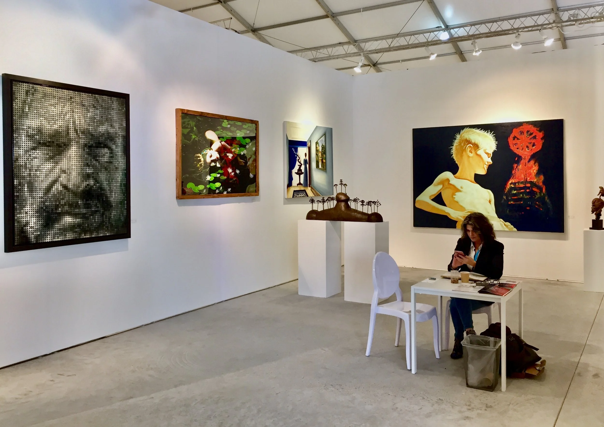 Conde Contemporary's booth at Context Art Miami, with Stacy Conde seated pre-opening, featuring art works by Leonid Rotar, José Bedia, Natasha Kertes, Andrés Conde, César Orrico and Darian Mederos.