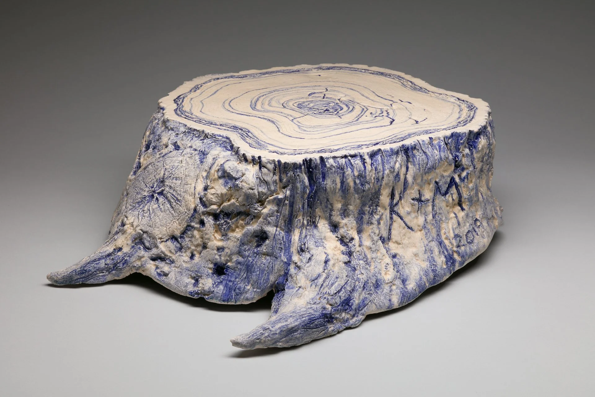 A blue and white ceramic sculpture by American artist Kevin Sloan, titled Lover's Stump, featuring a tree stump with lover's initials carved into the bark, available at Conde Contemporary.