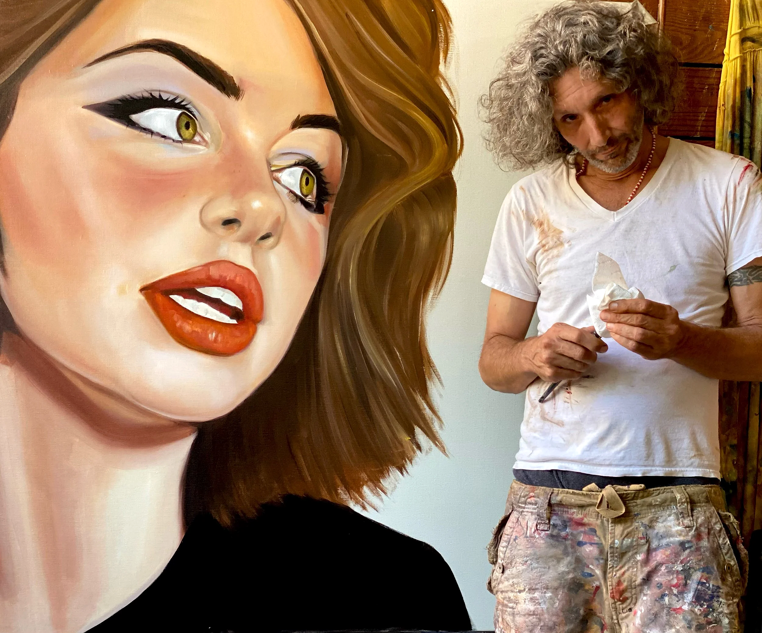 A photograph of the contemporary Cuban artist, living in Natchez, Andres Conde, standing beside his pop realist painting I Heard, the artist is represented by Conde Contemporary.