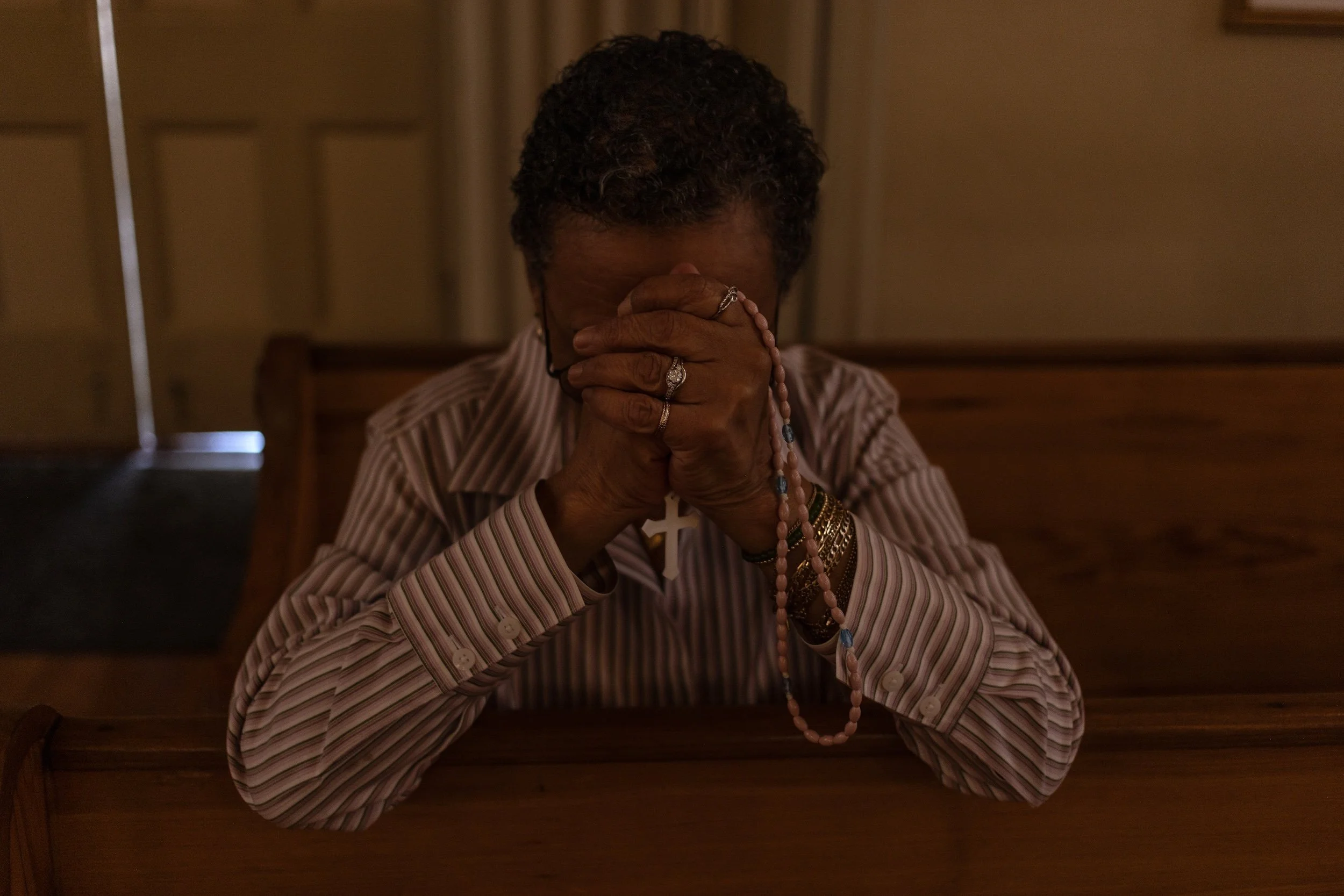 A color photo of a woman at St. Mary's Basilica in Natchez, Mississippi, holding a rosary and praying, photographed by photojournalist Alon Skuy for Conde Contemporary.