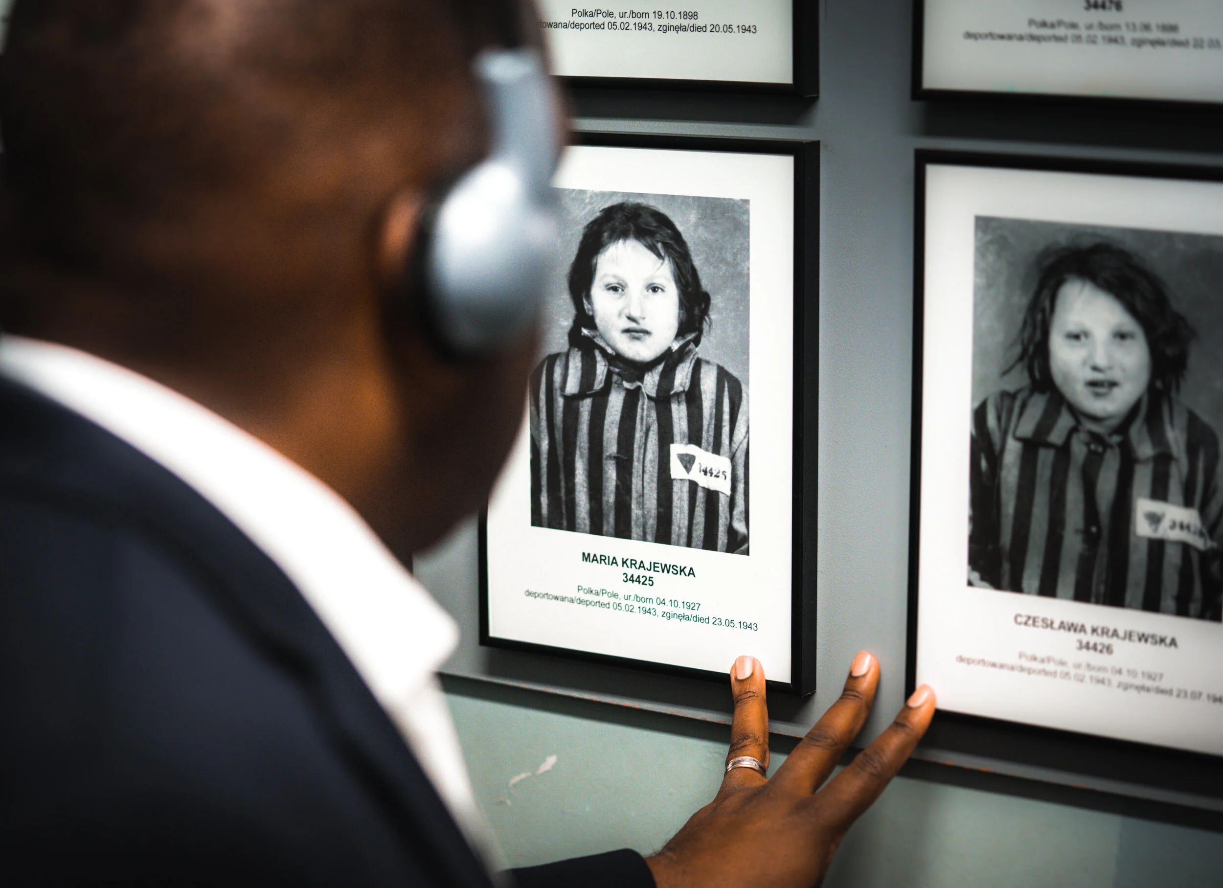 A person wearing headphones viewing a framed photograph of a concentration camp prisoner in black and white, with identification details on display.